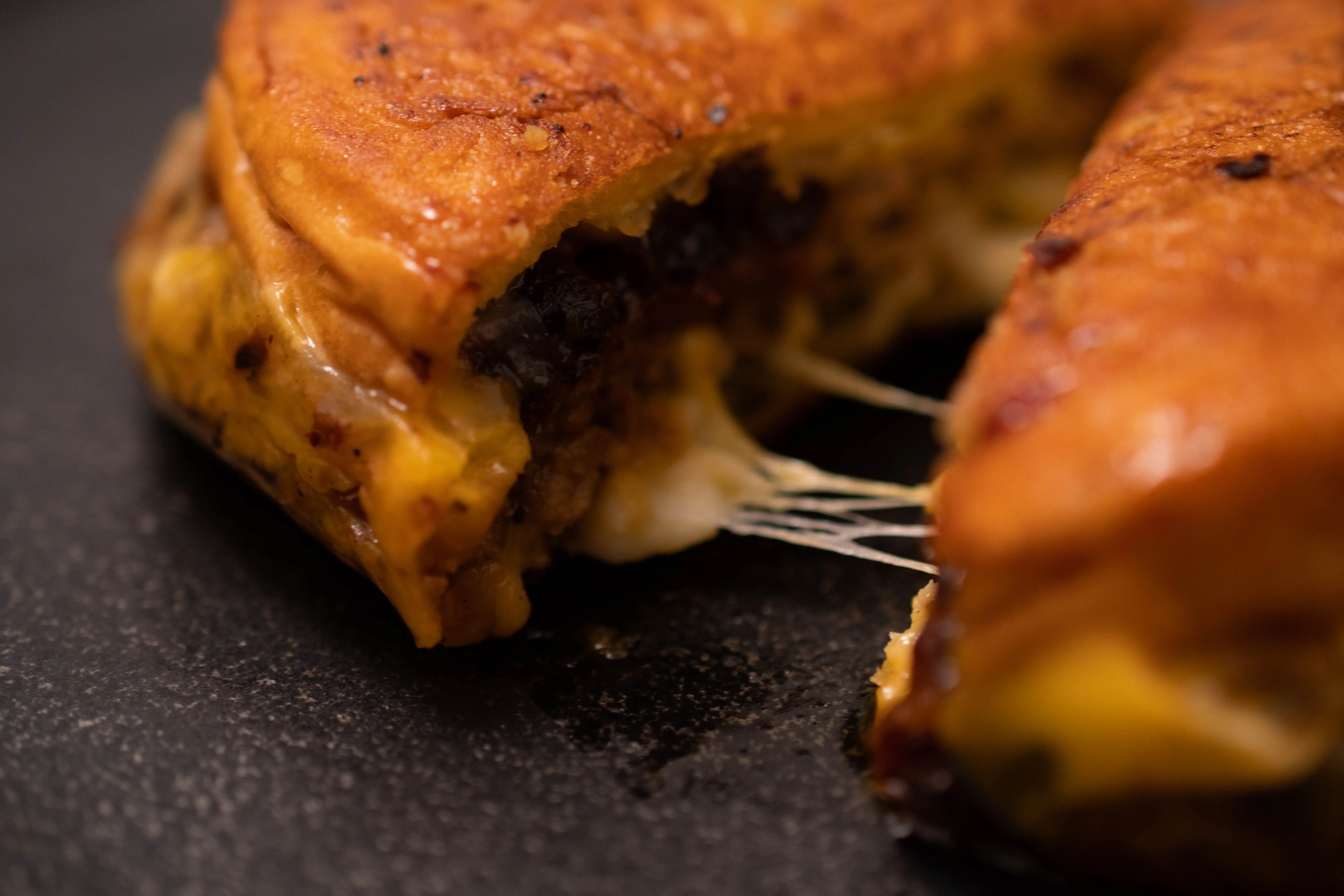 Closeup image of a burger cut in half with a cheese pull stretched between halves.