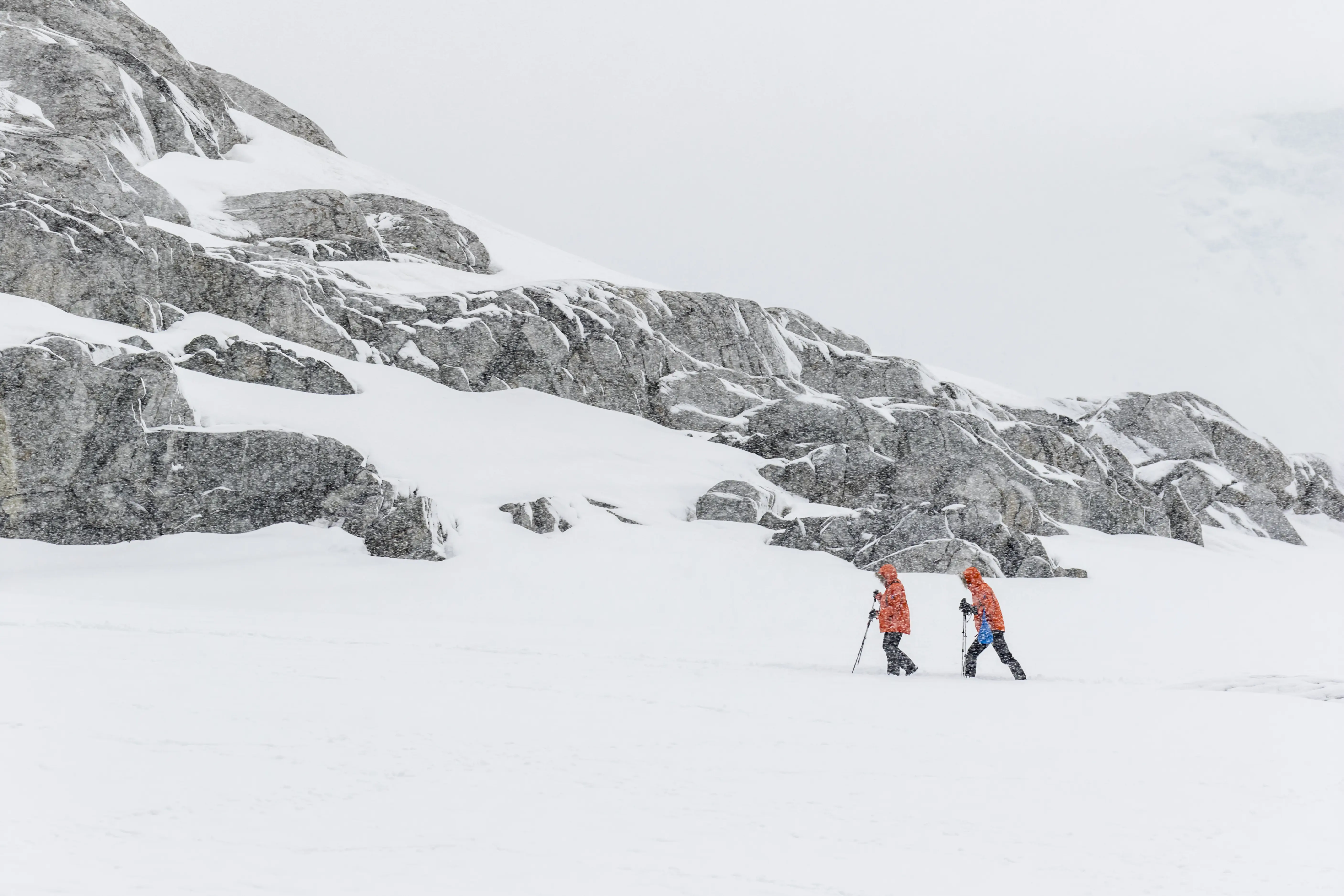 Image of two people in orange jackets walking in a snowstorm on Petermann Island, Antarctic Peninsula.