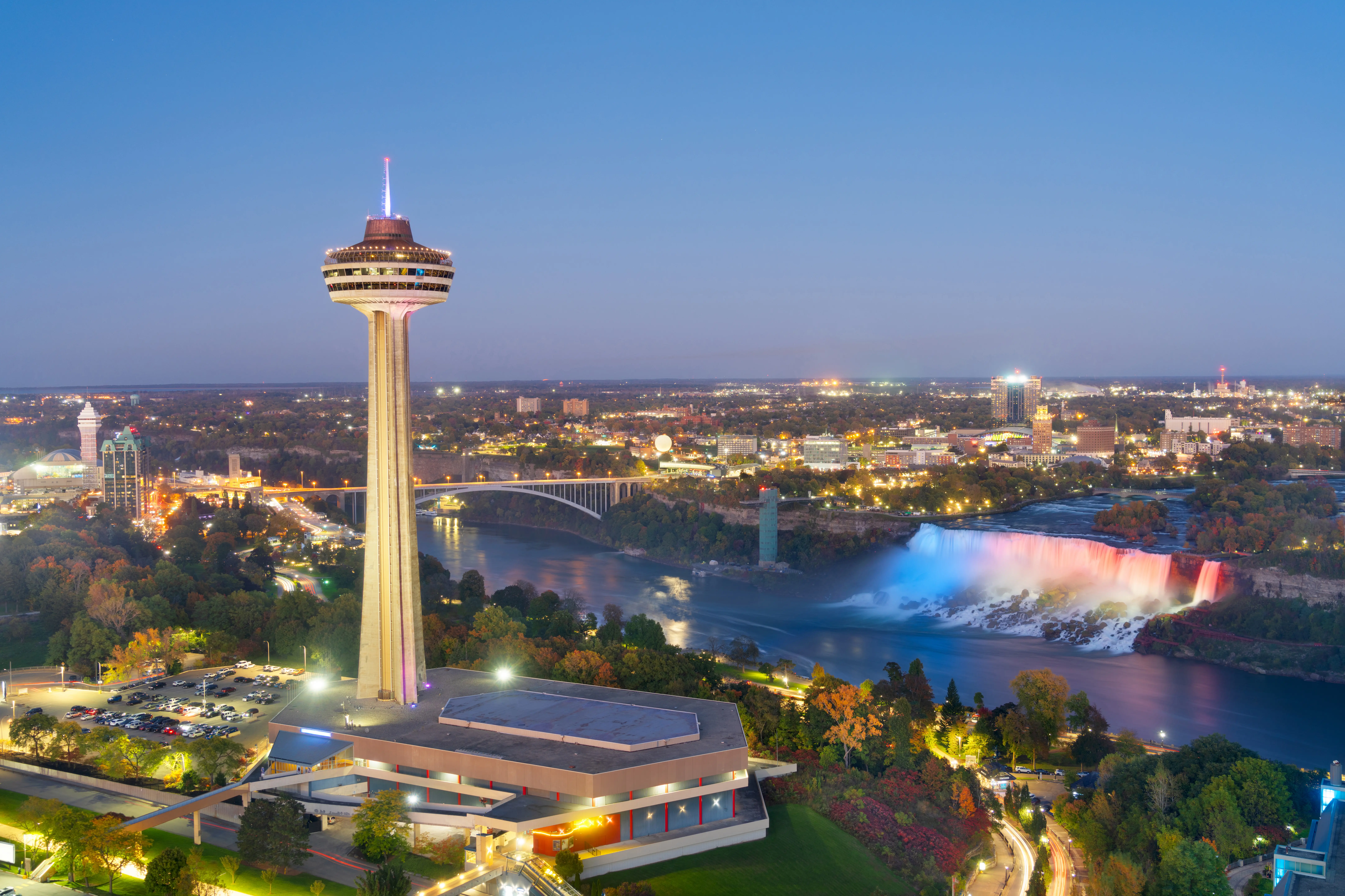 Ontario side of Niagara Falls with arial view of the falls, river, and Skylon Tower at dusk in Canada