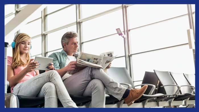 Two passengers entertaining themselves with a newspaper and an online game. 