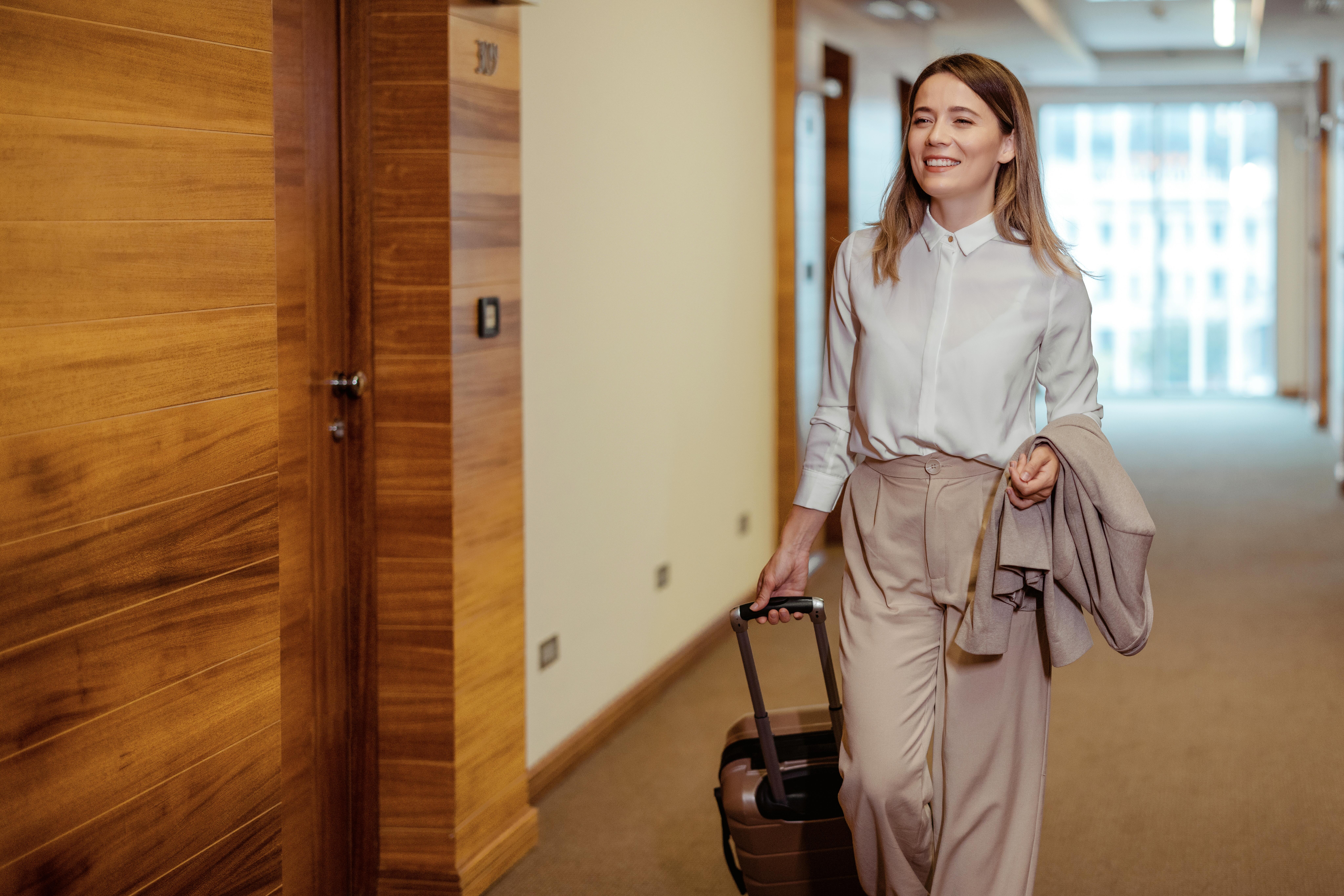 Young woman looking for her hotel room in hotel hallway with luggage