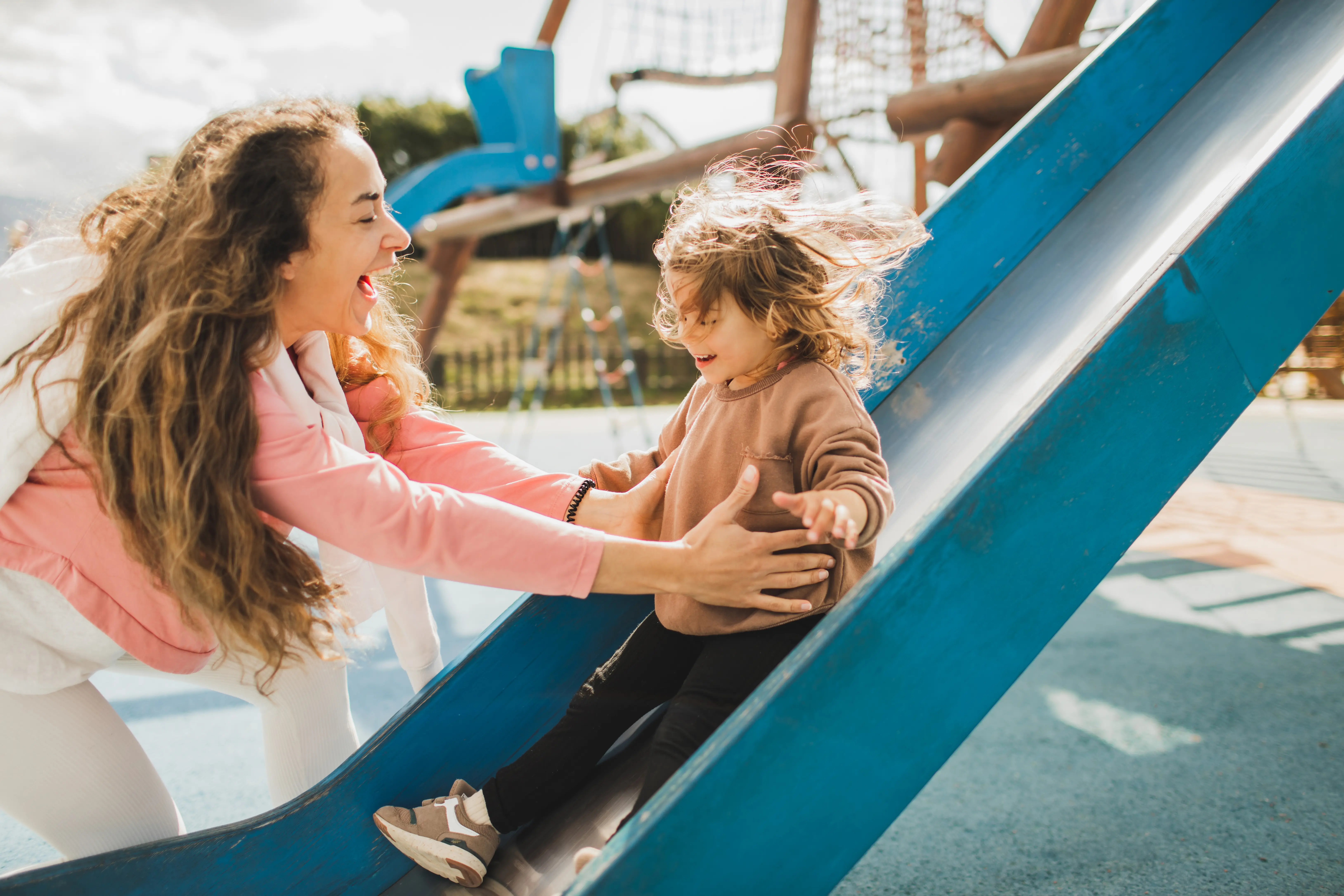 Image of a child going down a playground slide as the mother supervises.
