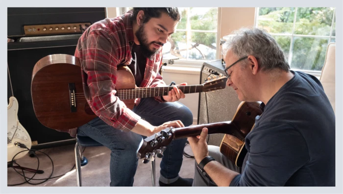 A guitar teacher and his student sit holding guitars during a guitar lesson.