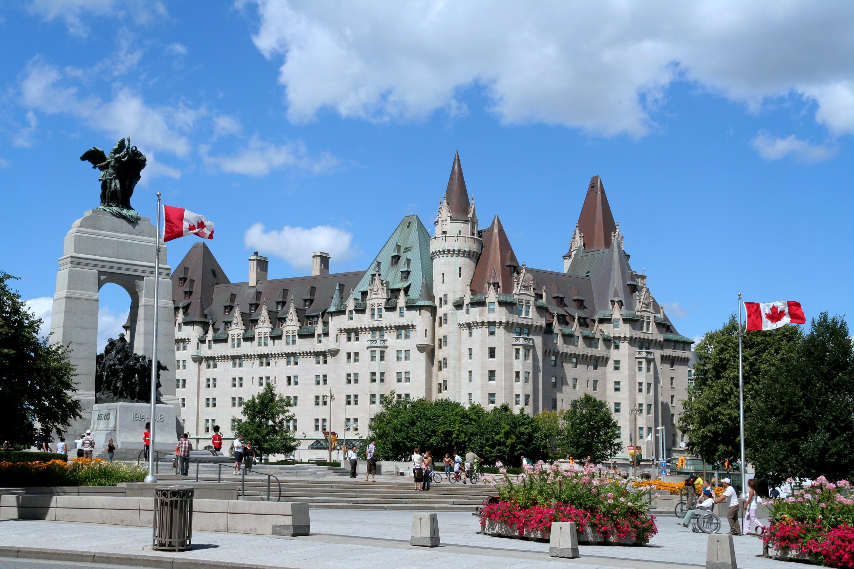 Sunny day view of the historic Fairmont Chateau Laurier hotel in the background and an arch shaped Cenotaph with remains of the unknown soldier on the left