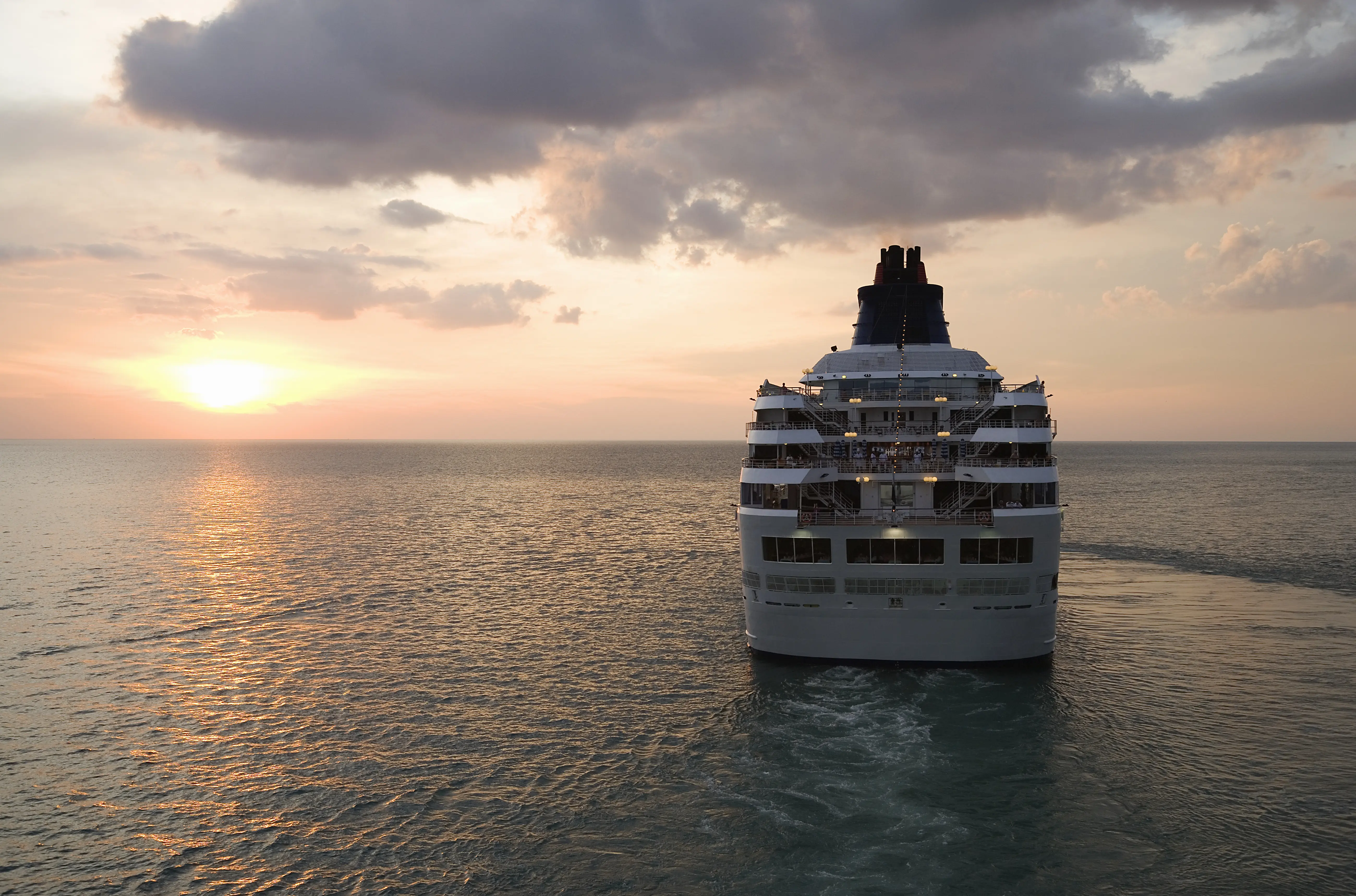 Image of a cruise ship sailing at dusk, with the setting sun visible.