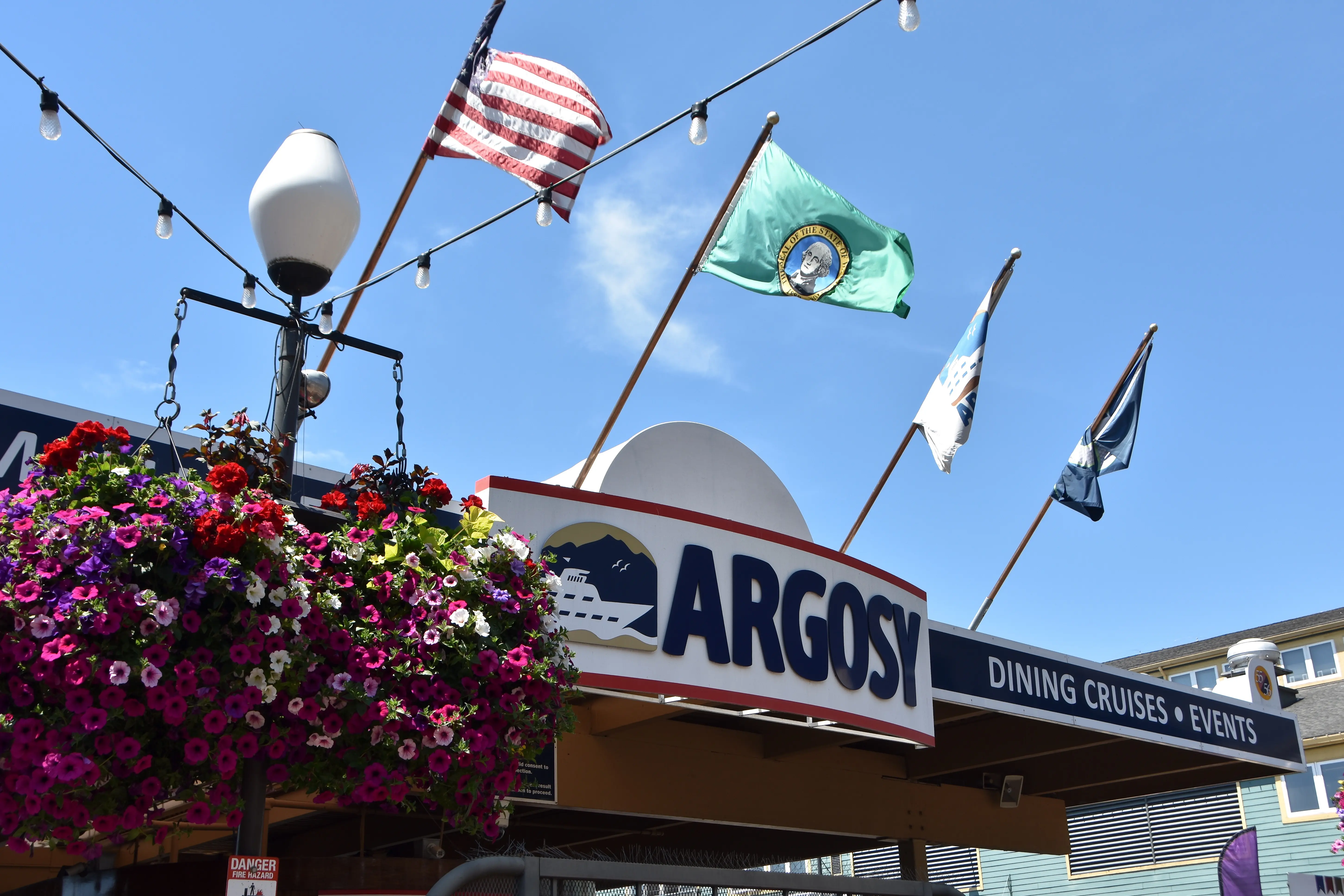Colorful hanging plants and flags with the sign for Argosy Dining Cruises and Events in Seattle, Washington.
