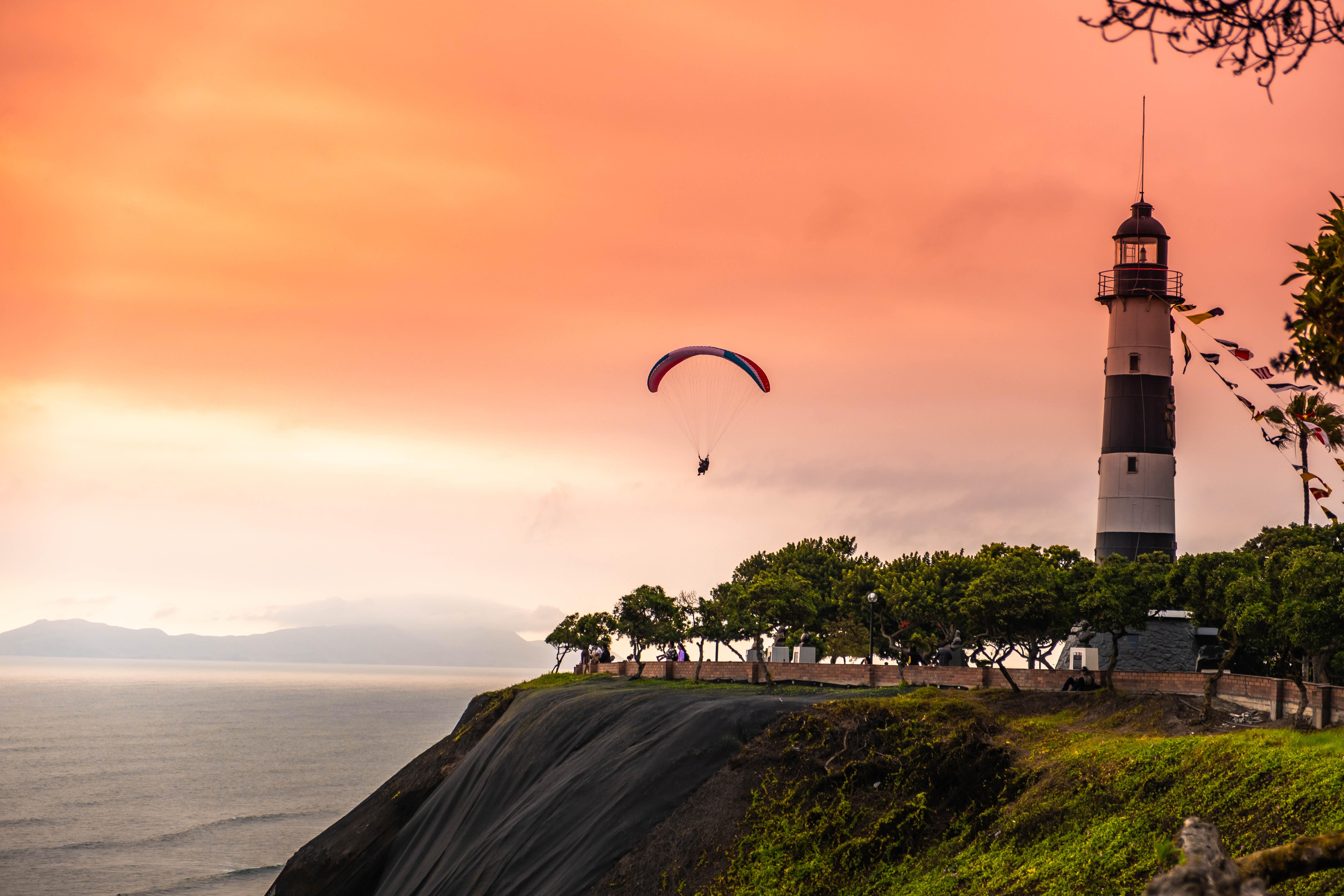Photo of a person parasailing by a lighthouse during sunset at the Port of Callao Lima, Peru