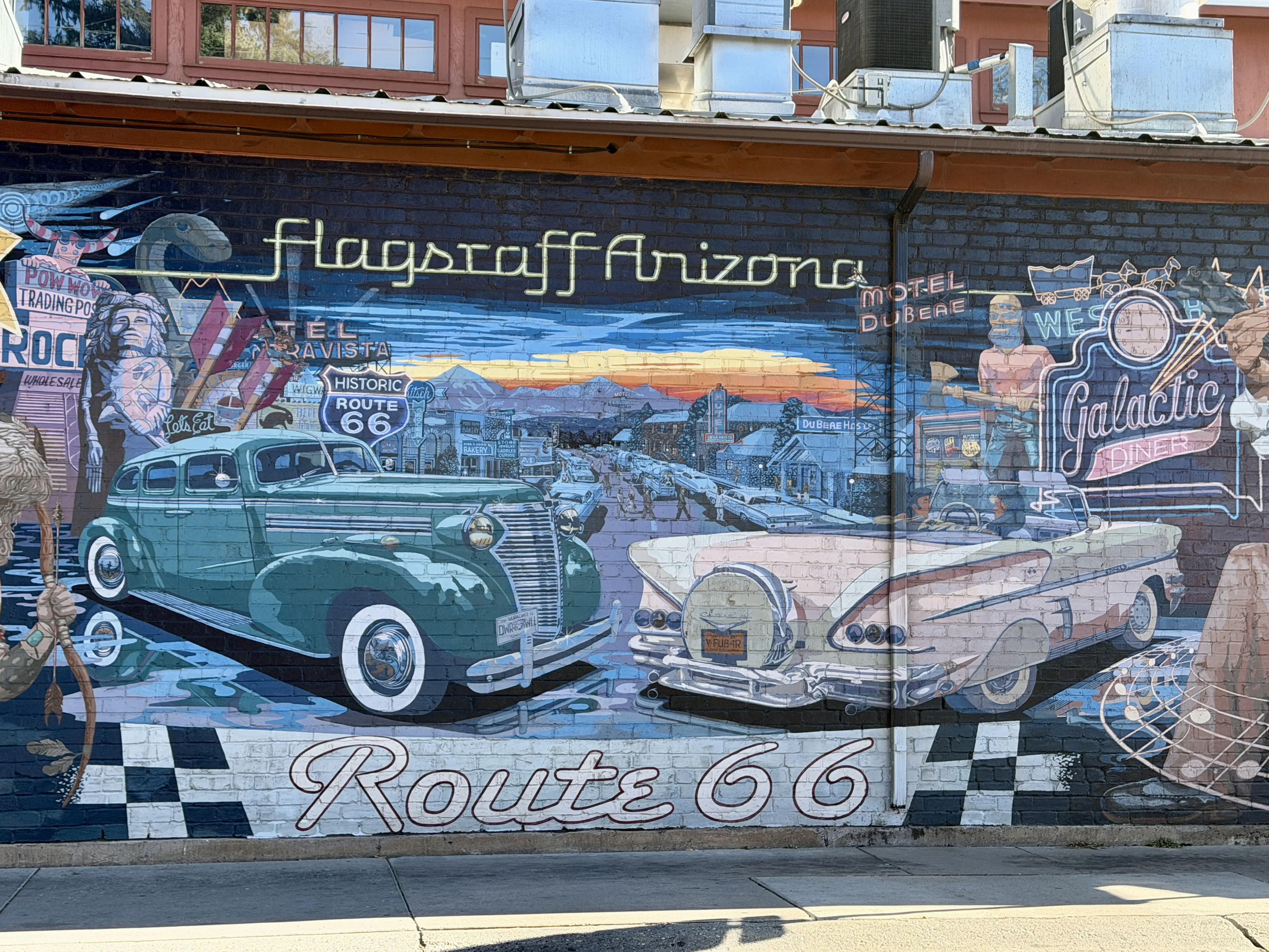 Mural painted on brick building features classic cars, neon signs and iconic Route 66 attractiona