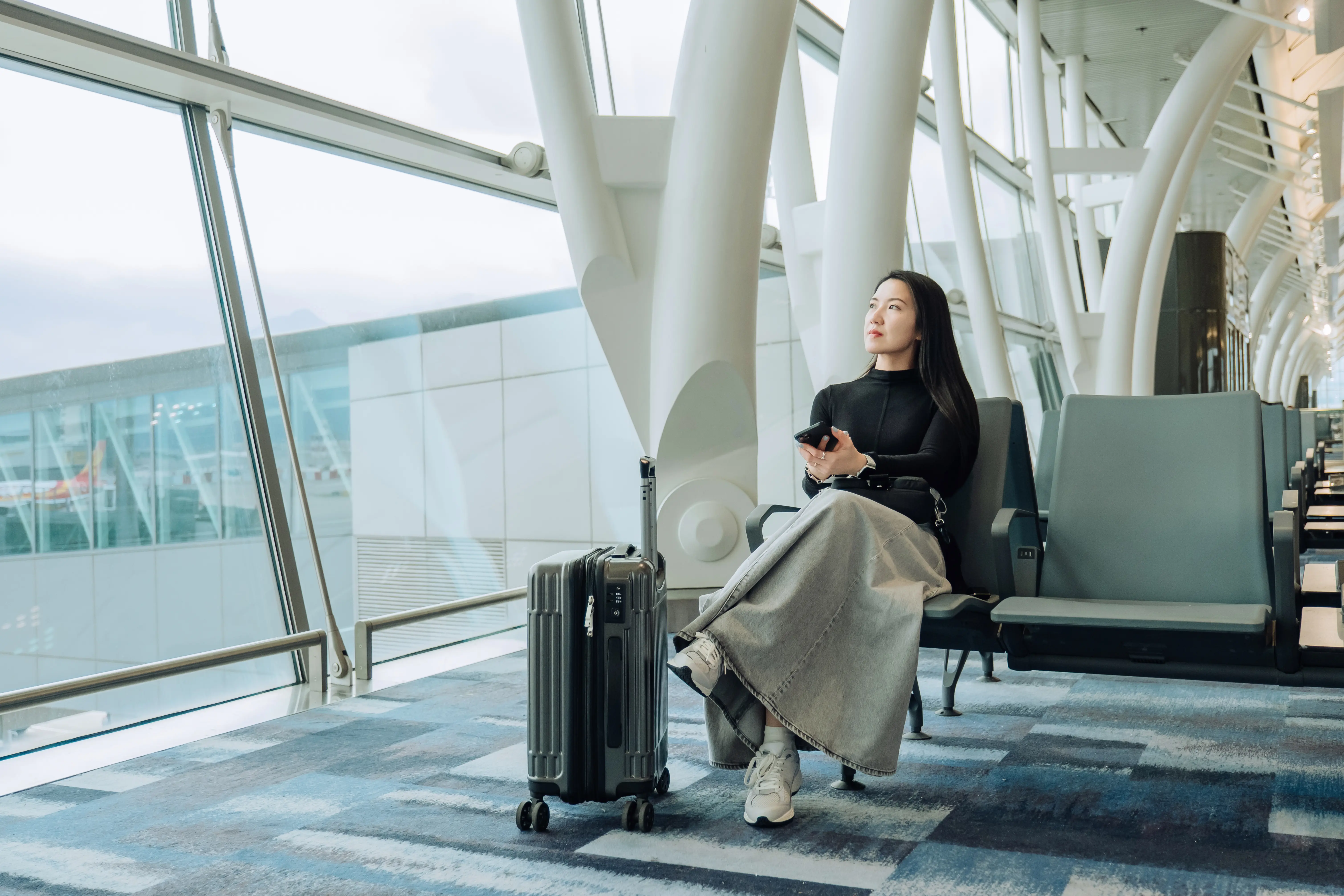 Image of a woman sitting at airport gate looking at planes outside the window.