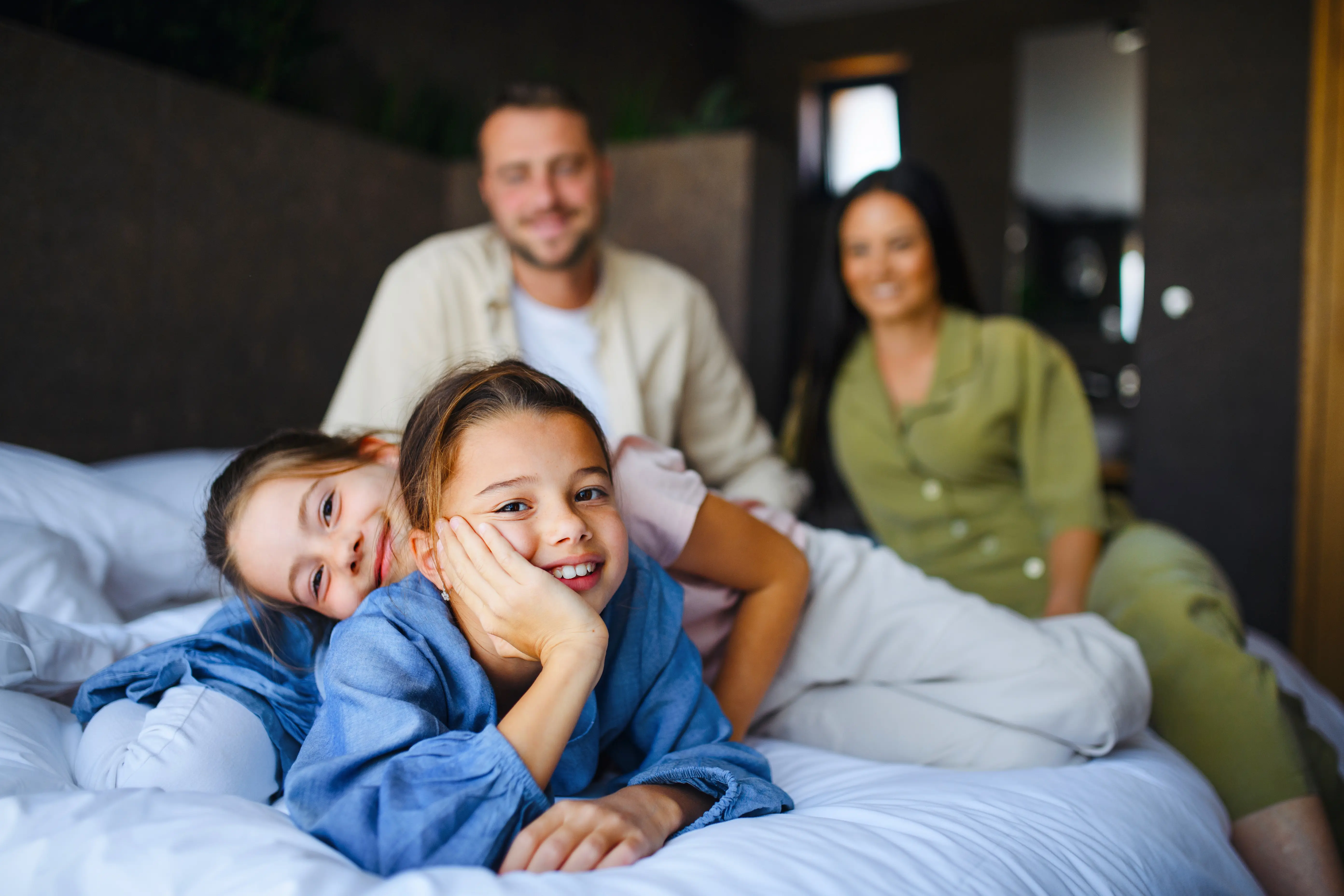 Family on summer holiday in hotel room with two young girls in foreground, parents in background