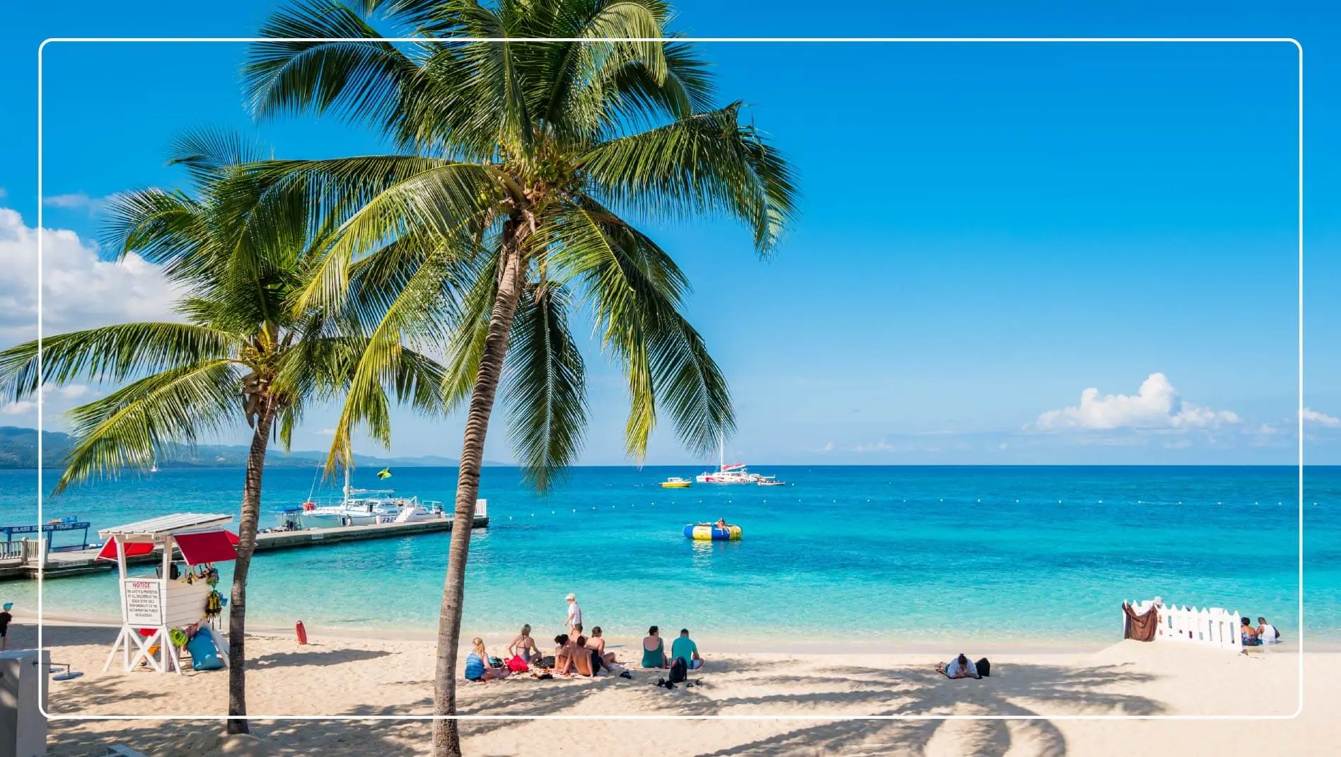 A family sits in the shade of a palm tree on a beach in Jamaica.