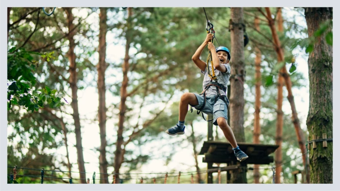 A girl is shown mid-air as she ziplines through a forest. 