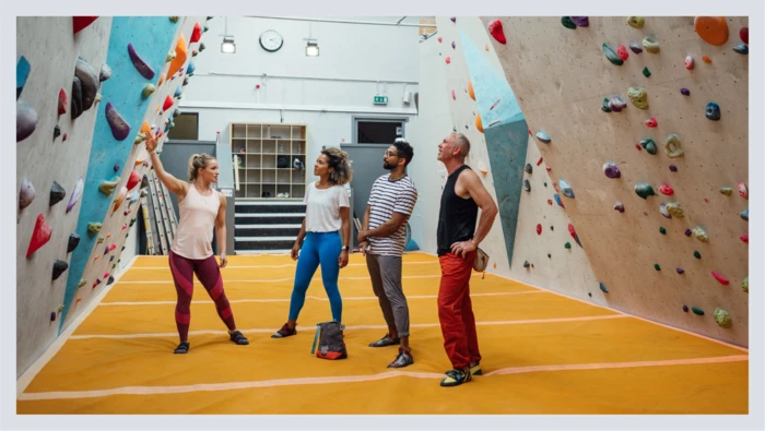 A group of friends at a rock climbing gym listen to an instructor before they go indoor rock climbing. 