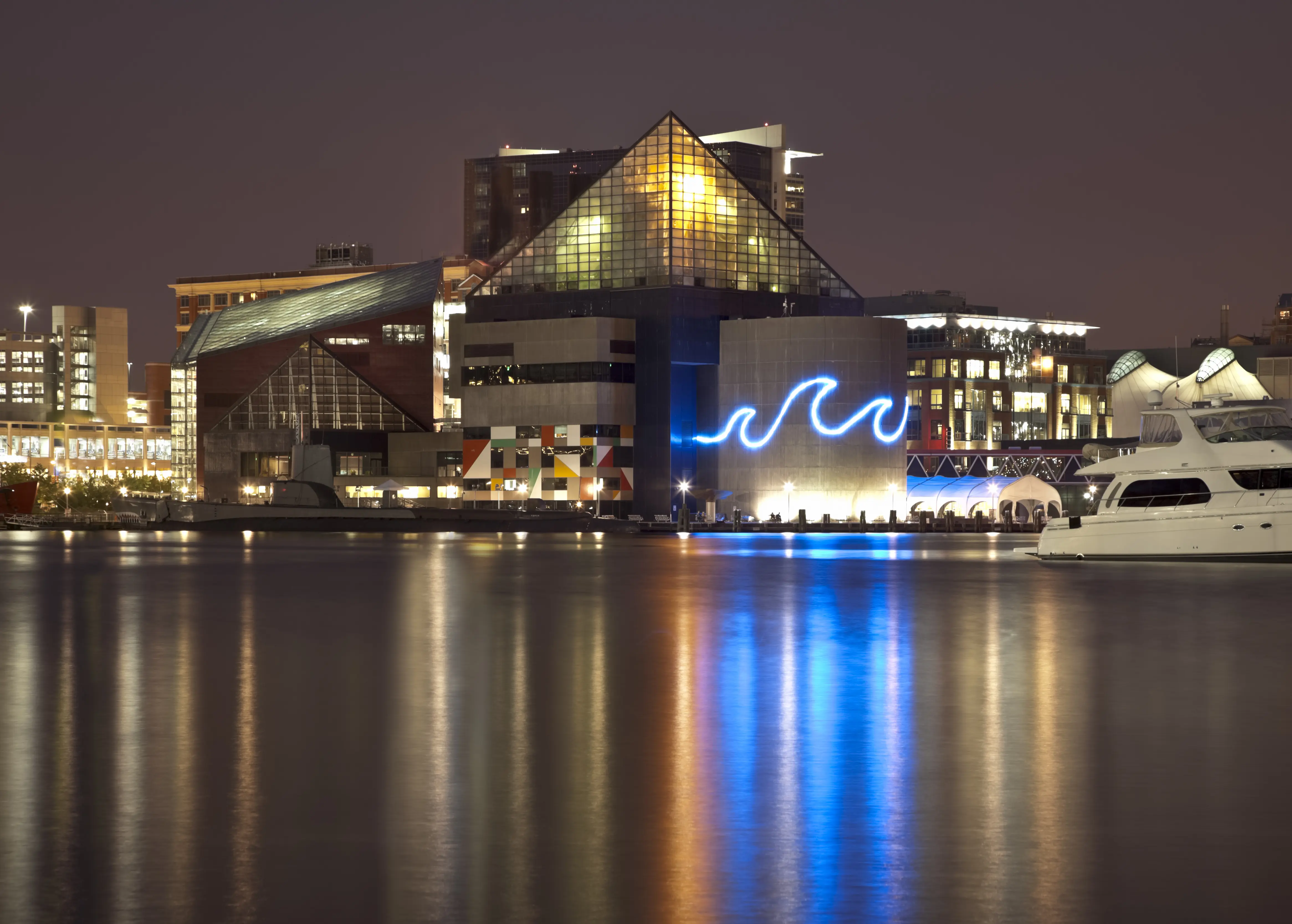 Baltimore's Inner Harbor cityscape at night with low clouds. The National Aquarium is aglow casting beautiful reflections on the calm water of the harbor.