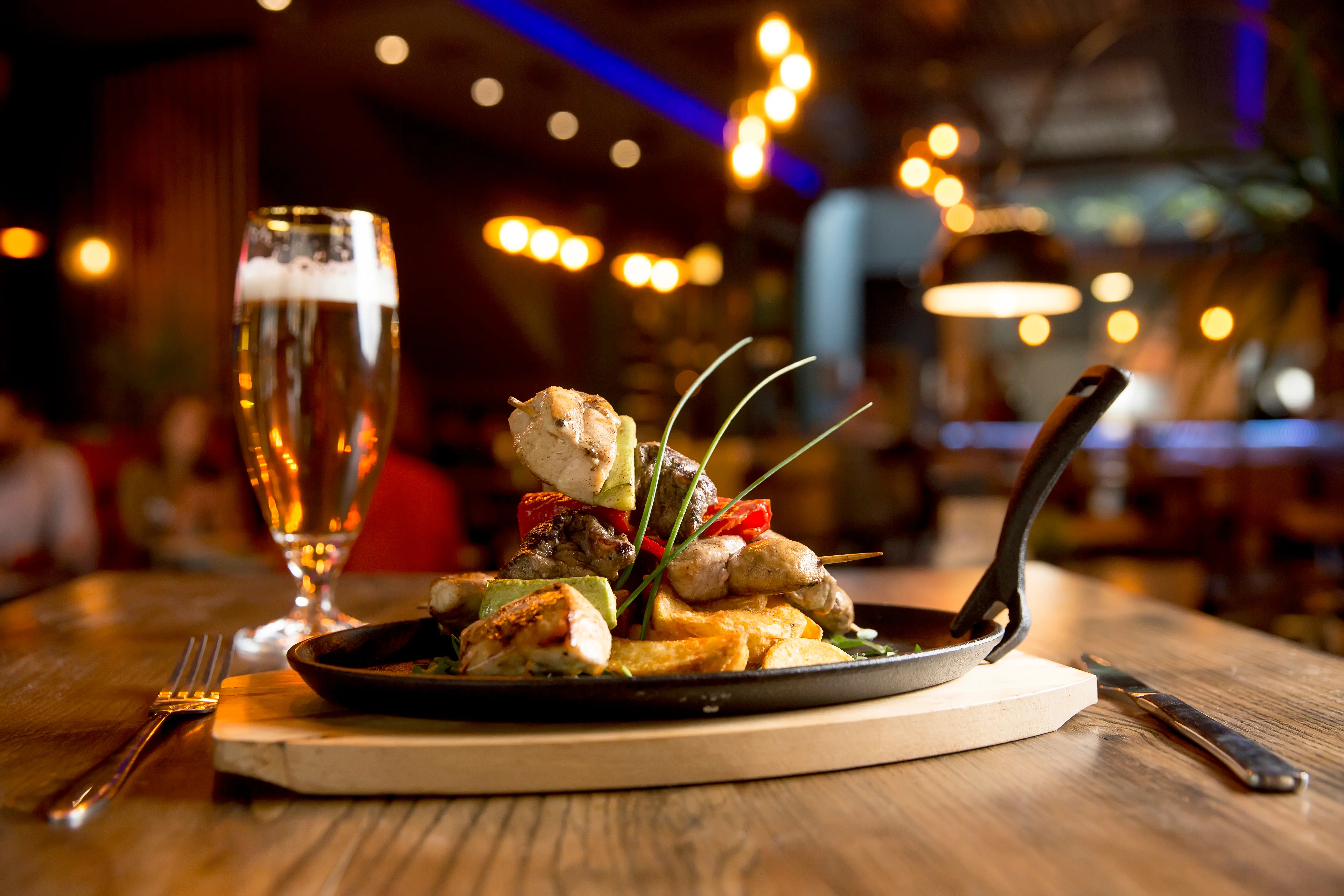 Chicken, pork and beef meat skewers with vegetables and spicy potatoes on the table in a cozy pub setting with warm lighting
