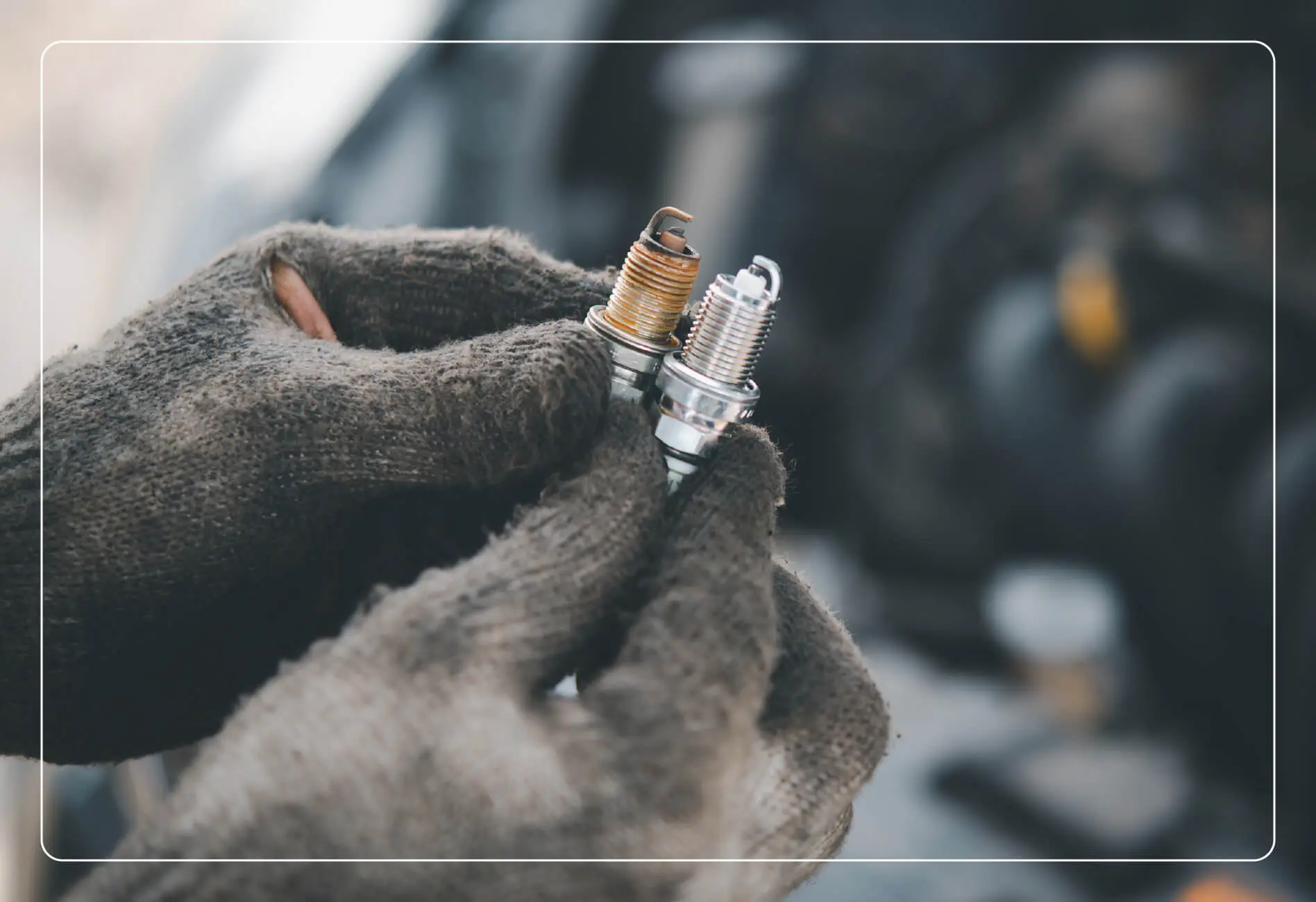 Hands with black gloves on holding 2 car spark plugs.
