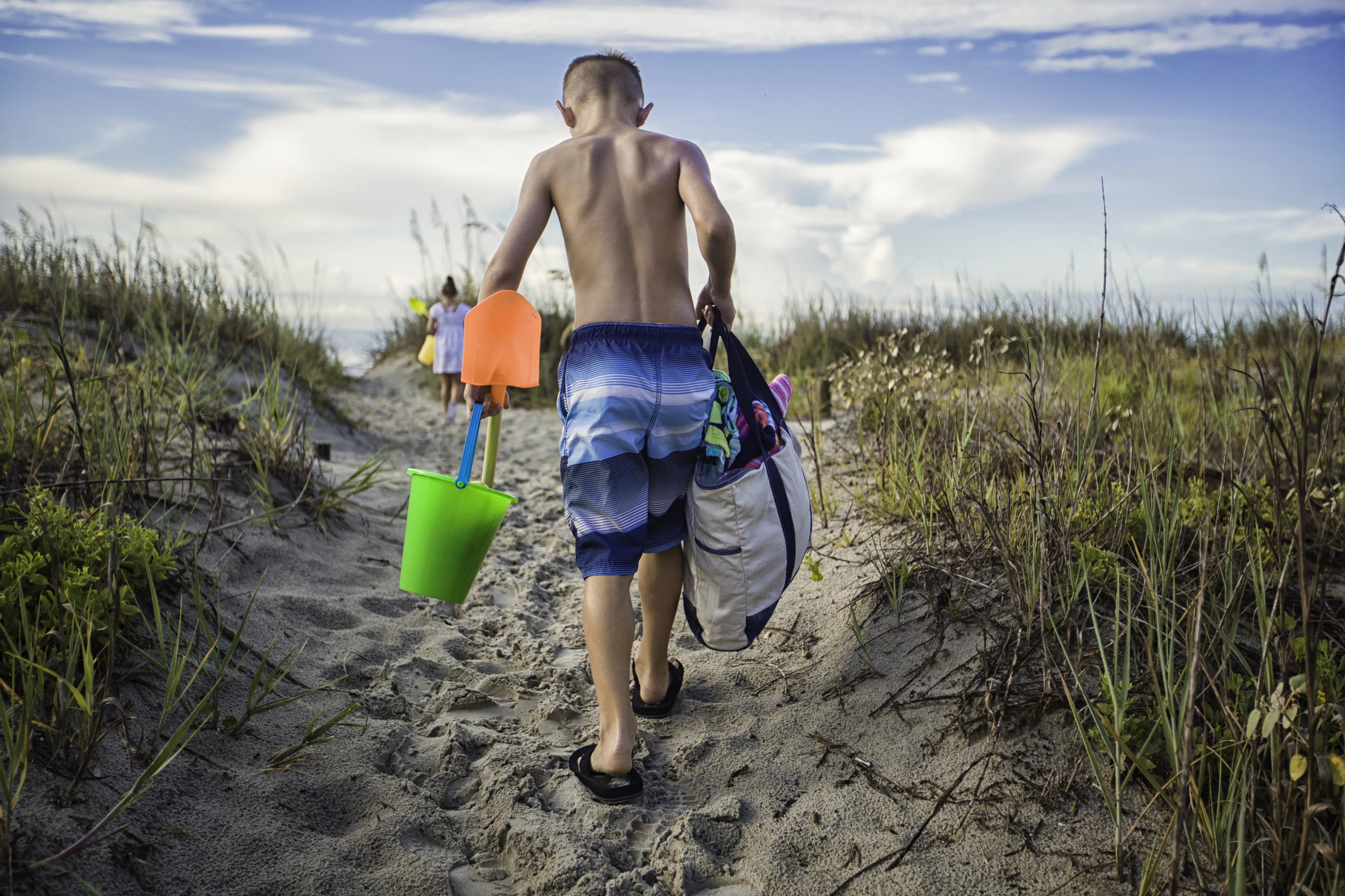 Image of a child carrying various beach supplies while walking to the shore.