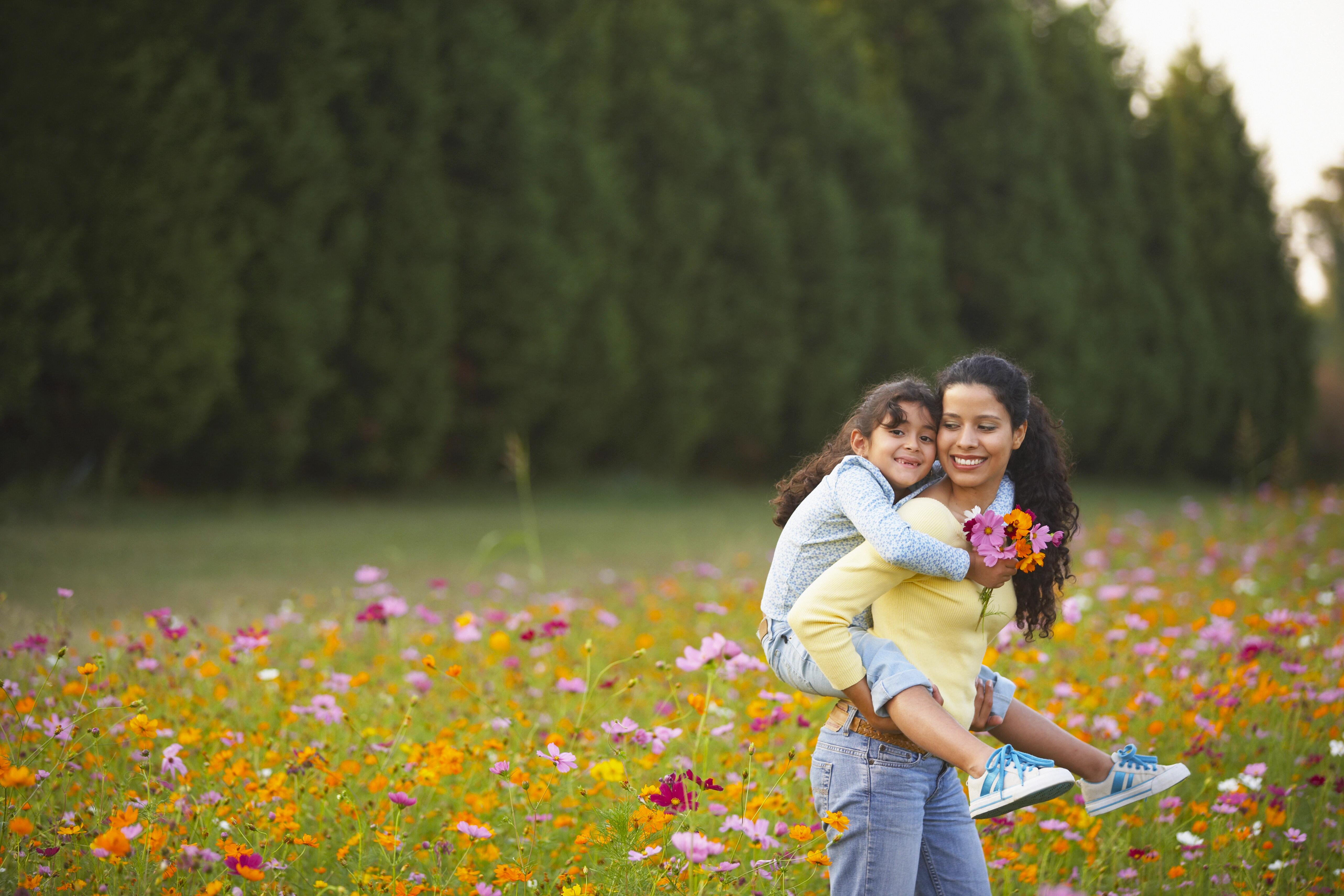 Mother giving daughter piggy back ride in field of flowers in the springtime