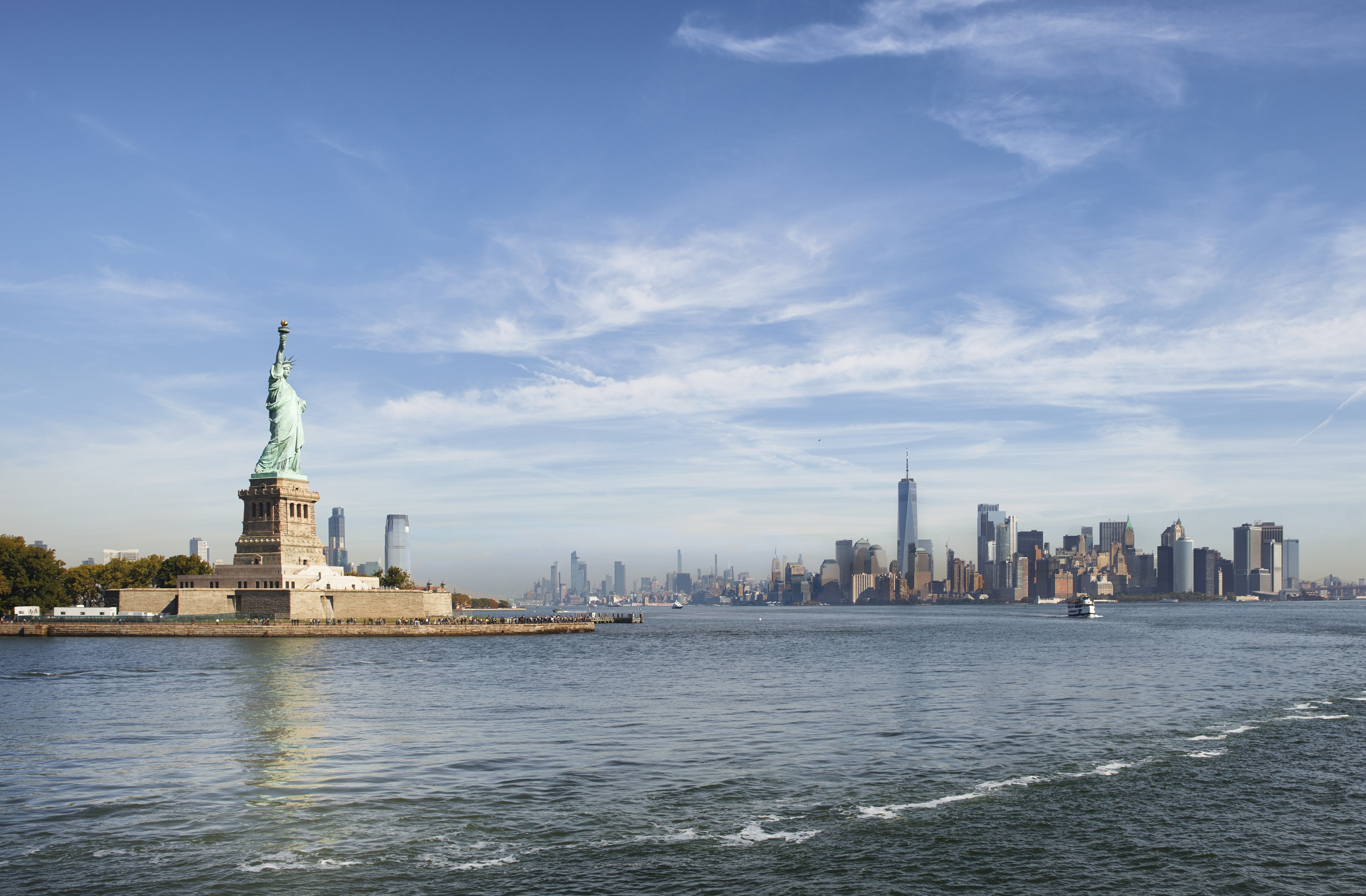 Image of the Statue of Liberty on the Hudson River, with New York City visible in the background.