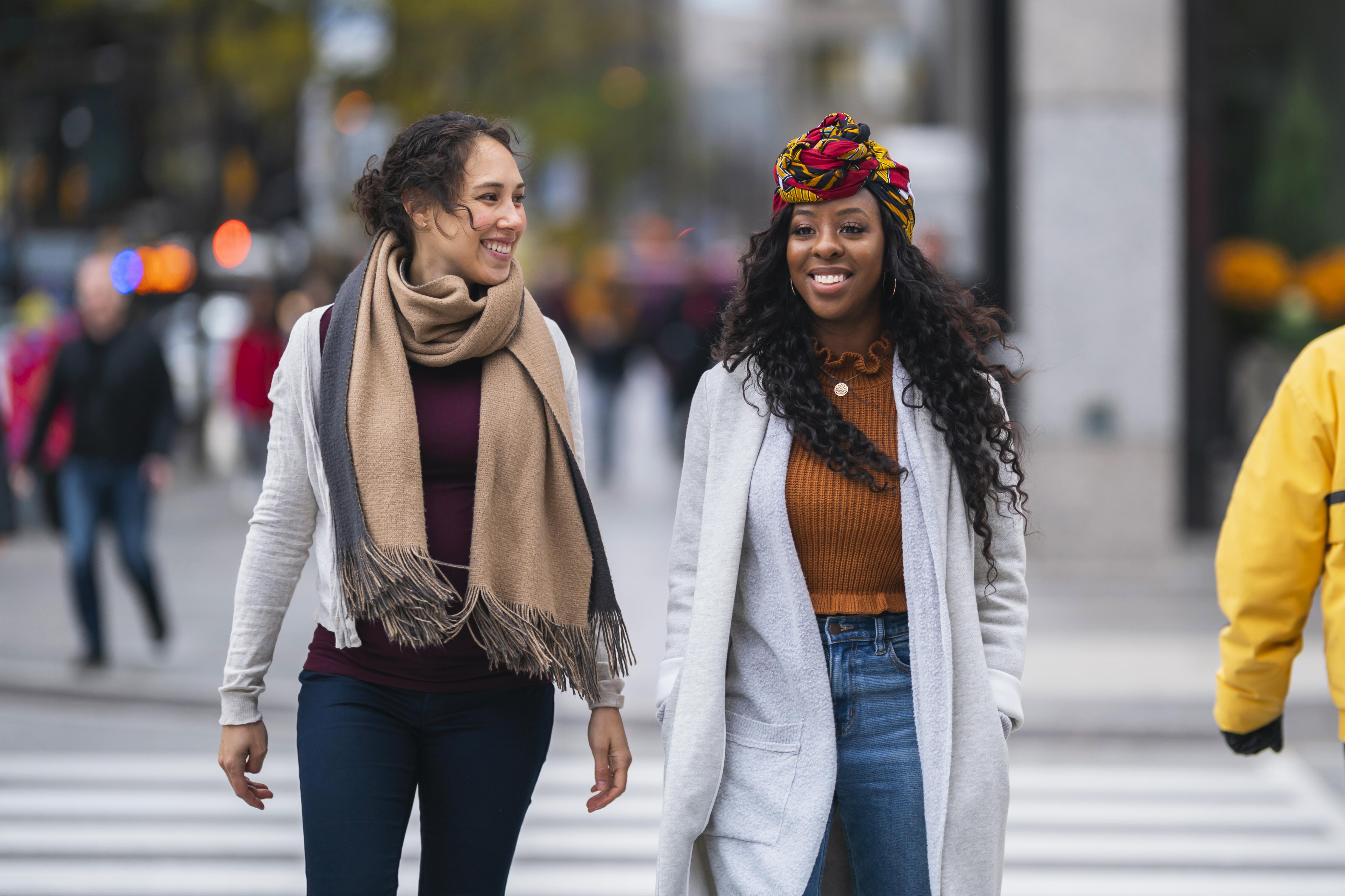 Two female friends walking and smiling through downtown Toronto