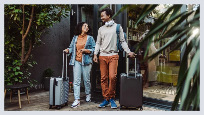 A couple holding their suitcases are shown entering an outdoor lobby at a hotel getaway.