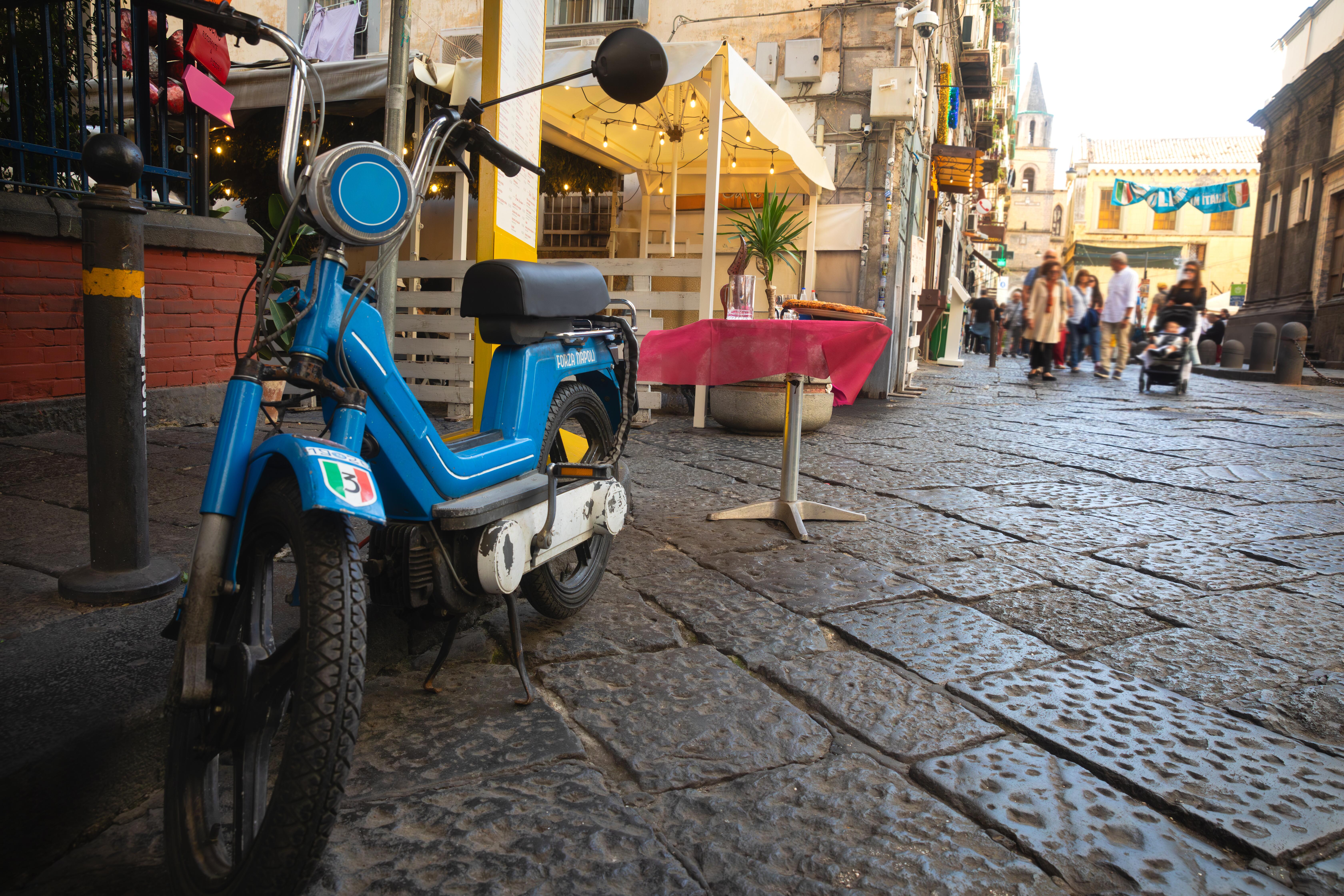 Naples city center with a vintage scooter in the foreground and group of people walking in the distance