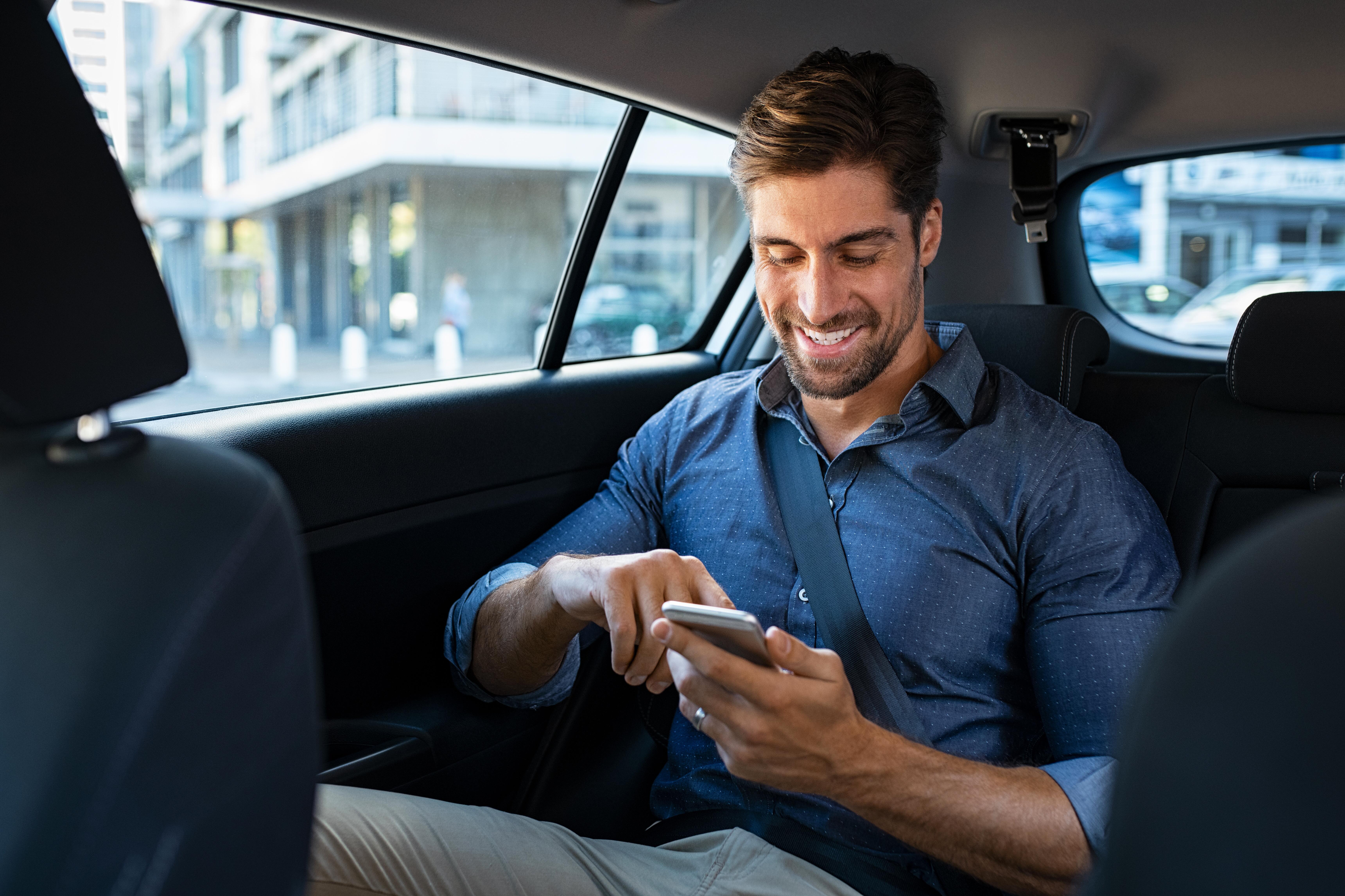 Man checking his phone while sitting in the back of a rideshare