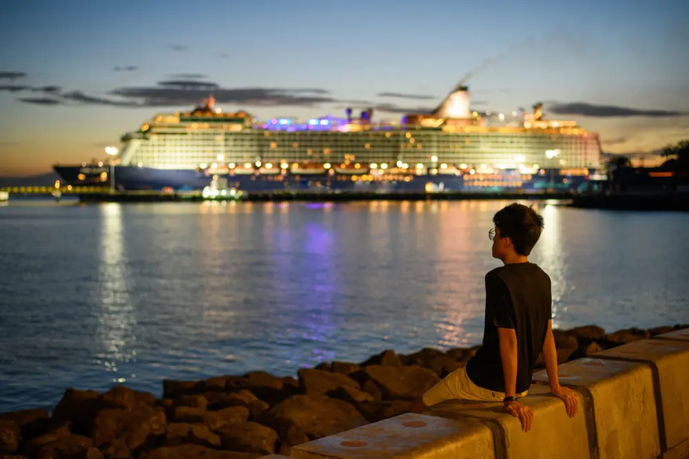 Man sitting on wall while looking at distant cruise ship