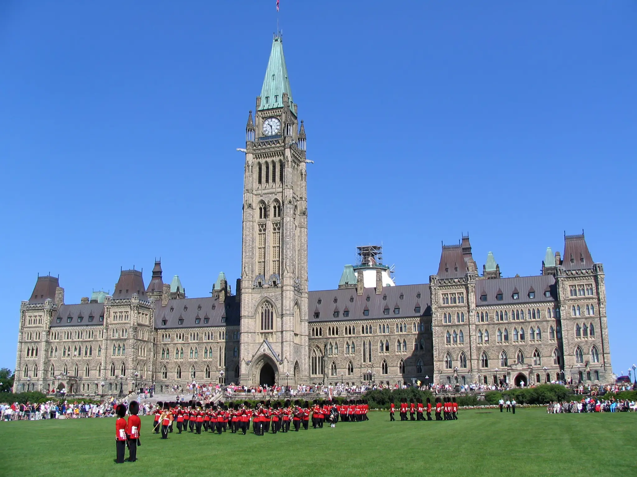 Changing of the guard ceremony in front of the Gothic Revival style Canadian Parliament building with architectural details including pointed arches, lancet windows, and intricate carvings