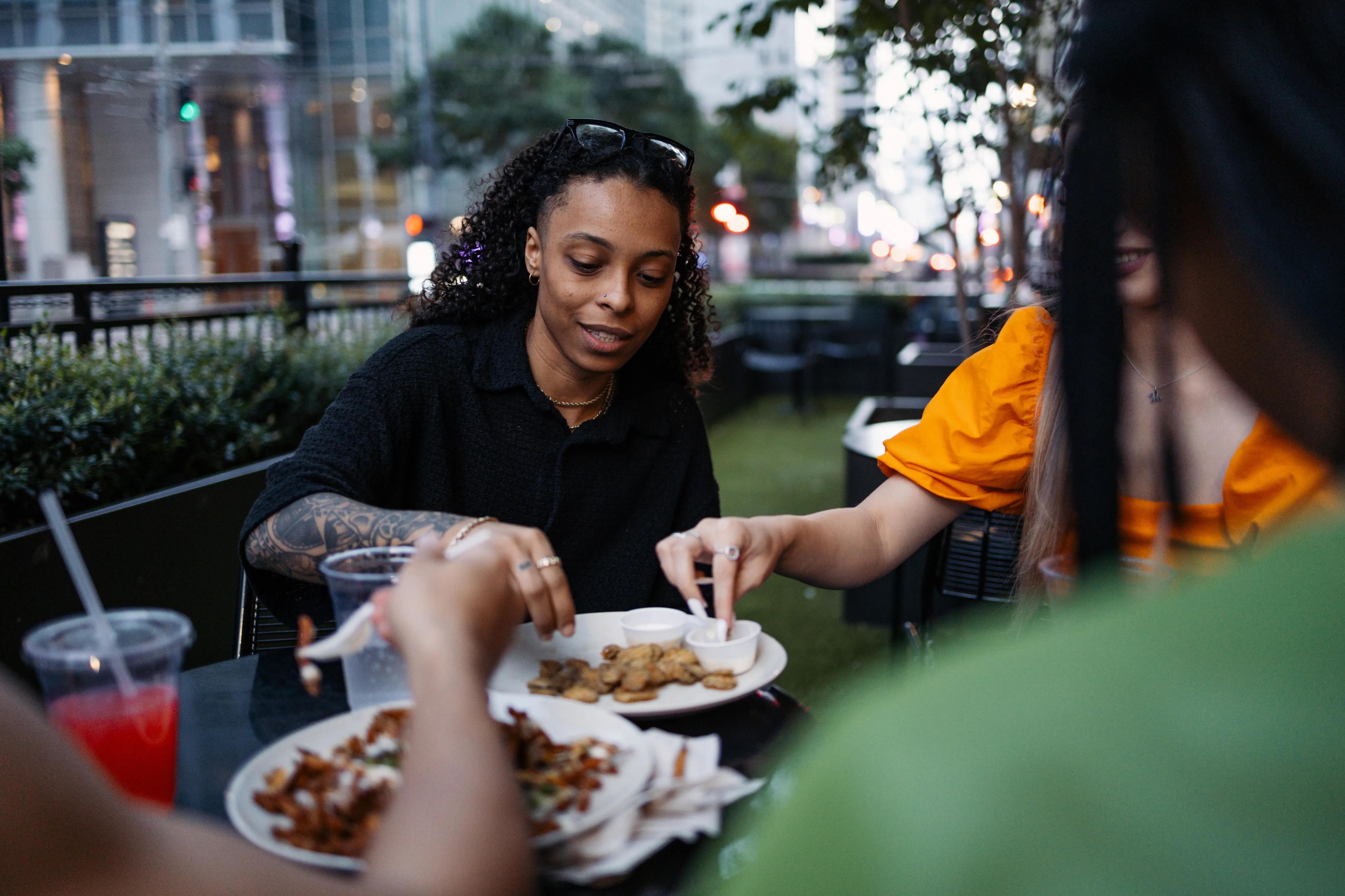 A group of friends share a meal and beverages outdoors in a busy city environment, highlighting camaraderie and urban dining culture.