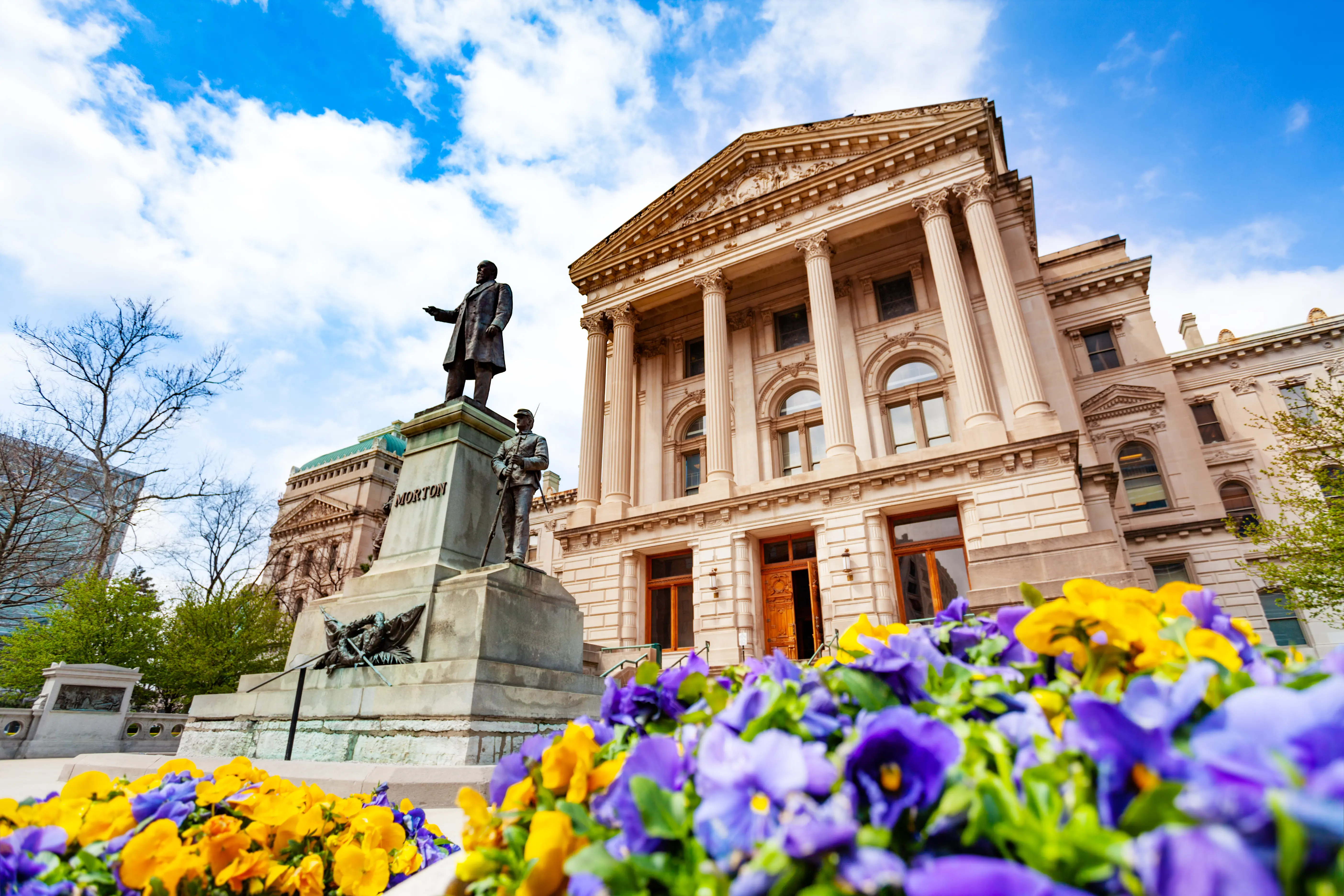 Oliver Perry Morton statue in front of the Indiana State Capitol building in springtime with purple and yellow flowers, Indianapolis, USA