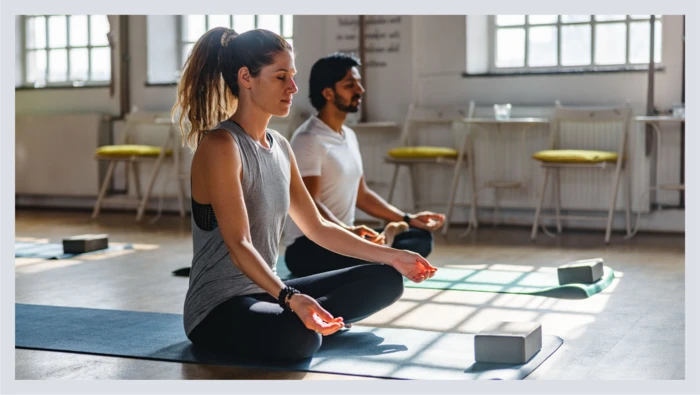 A couple sits on yoga mats meditating in a yoga class. 