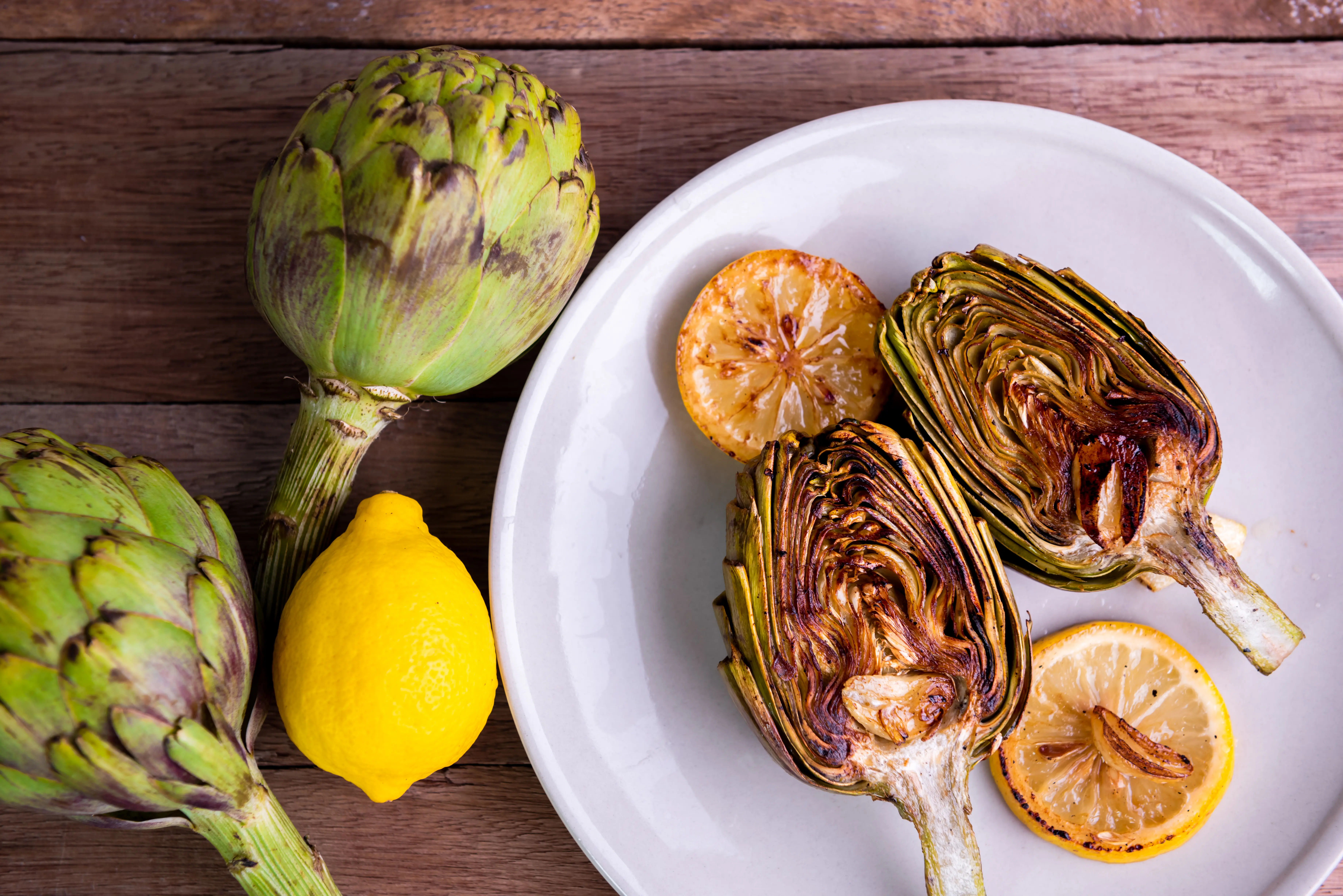 Image of roasted artichoke served on a plate with lemon slices.