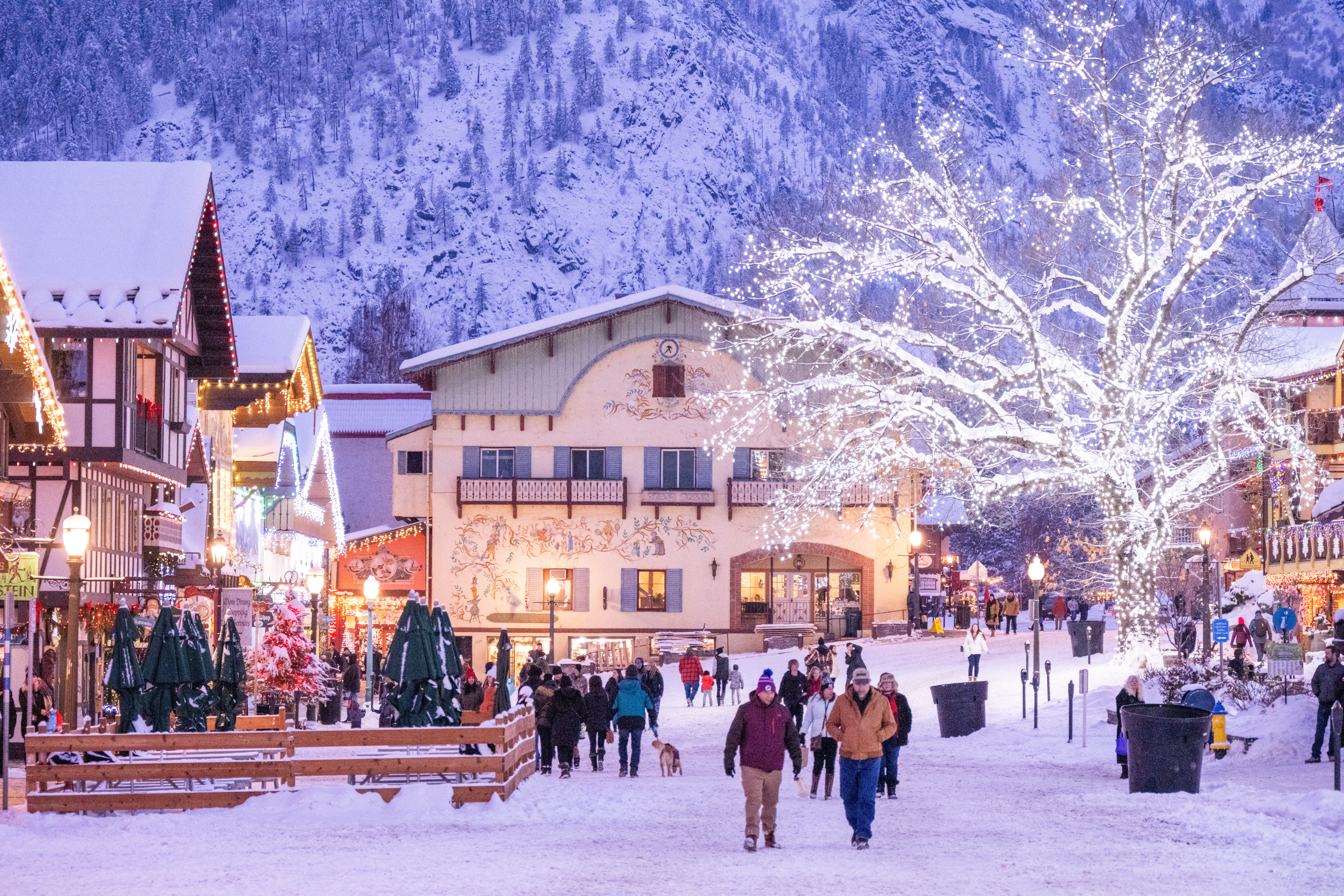 Snowy town square with lighted roof eves and trees with mountains in the background