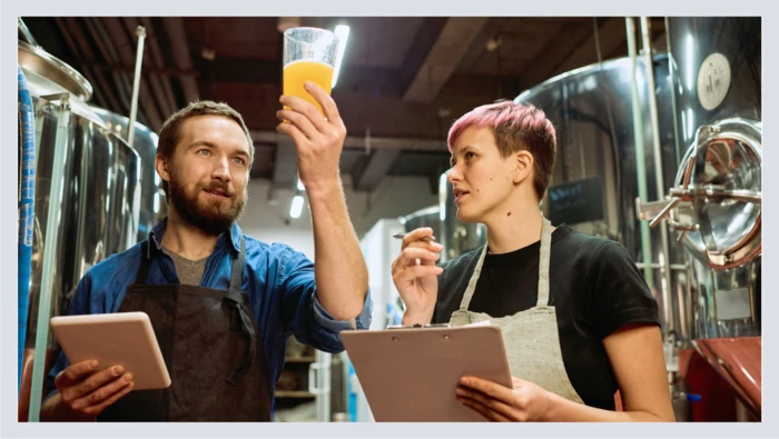 Two beer brewers assess a freshly made beer inside of a brewery.