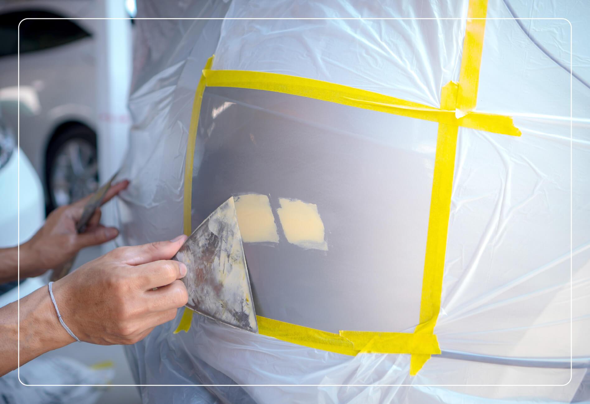 Someone patching dents on the back of a car with putty.