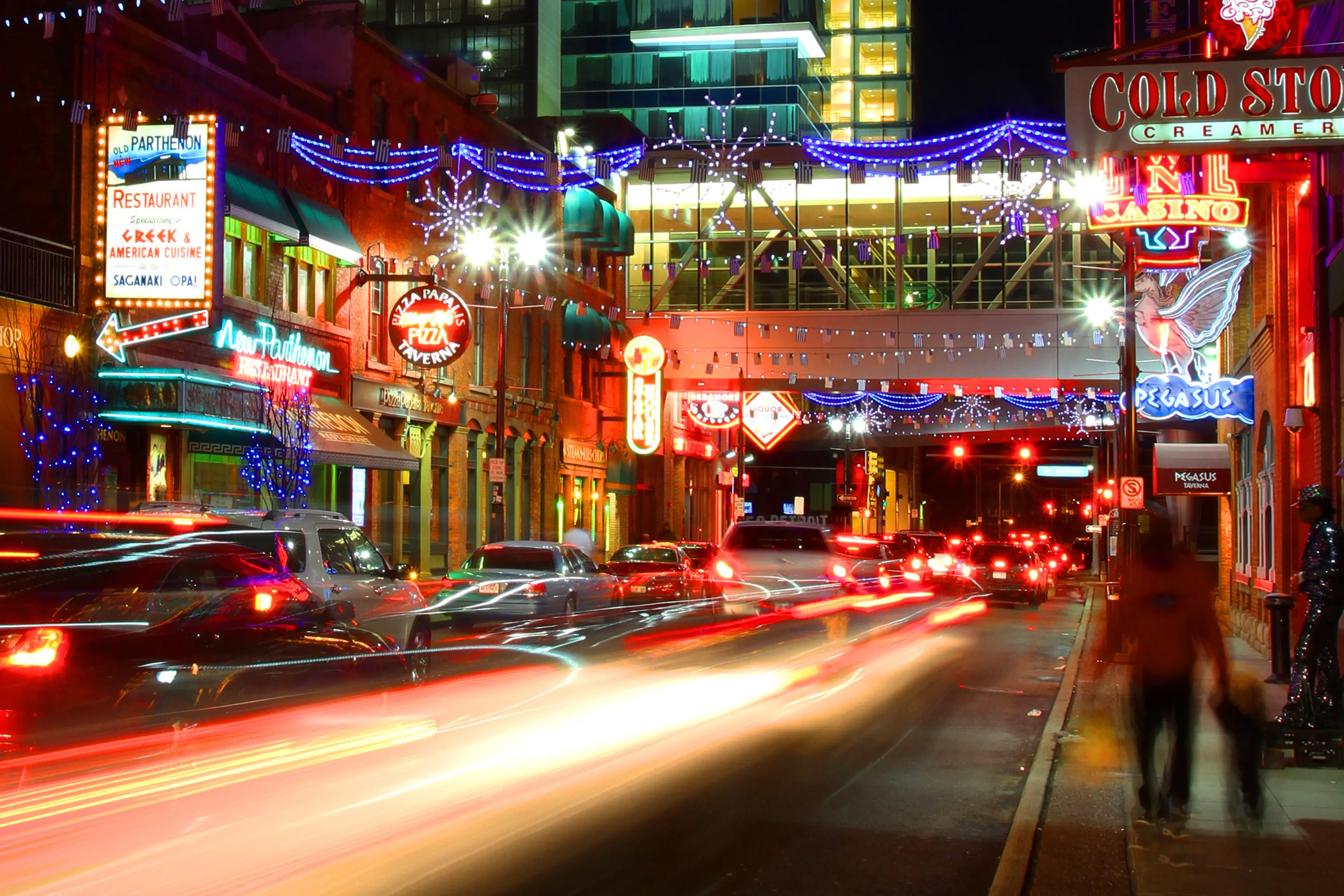 This is a long exposure picture of Monroe Avenue, the heart of the Greektown District in Detroit, Michigan. Due to the long exposure, vehicle lights streak through this dynamic image, and pedestrians become a blur. This highlights the nightlife and excitement of this entertainment district.