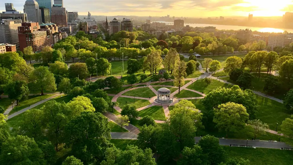 An aerial view of the Boston Common with the sun setting in the background.
