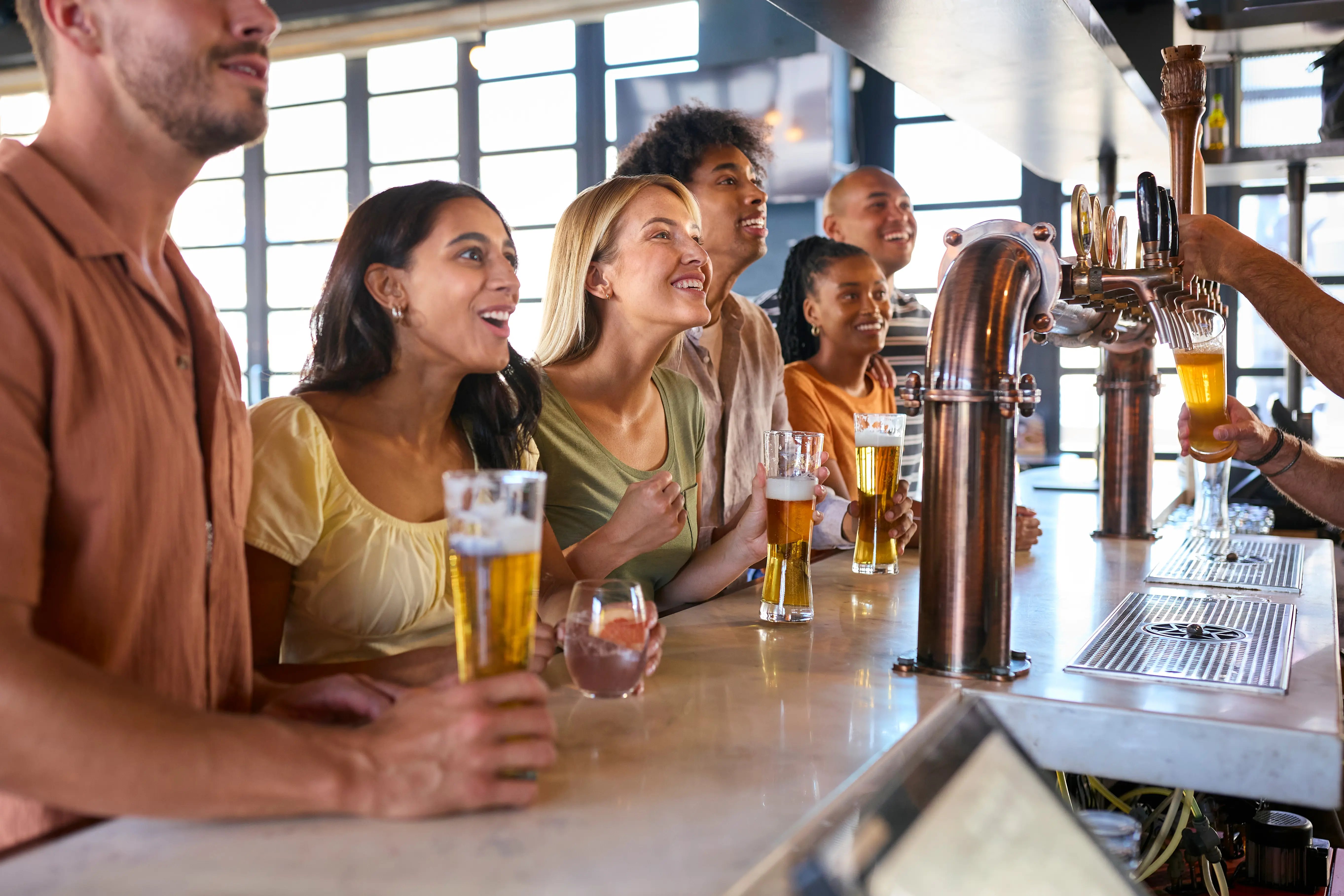 Multi-cultural group of friends in a sports bar or brewery celebrating as they watch a game on TV