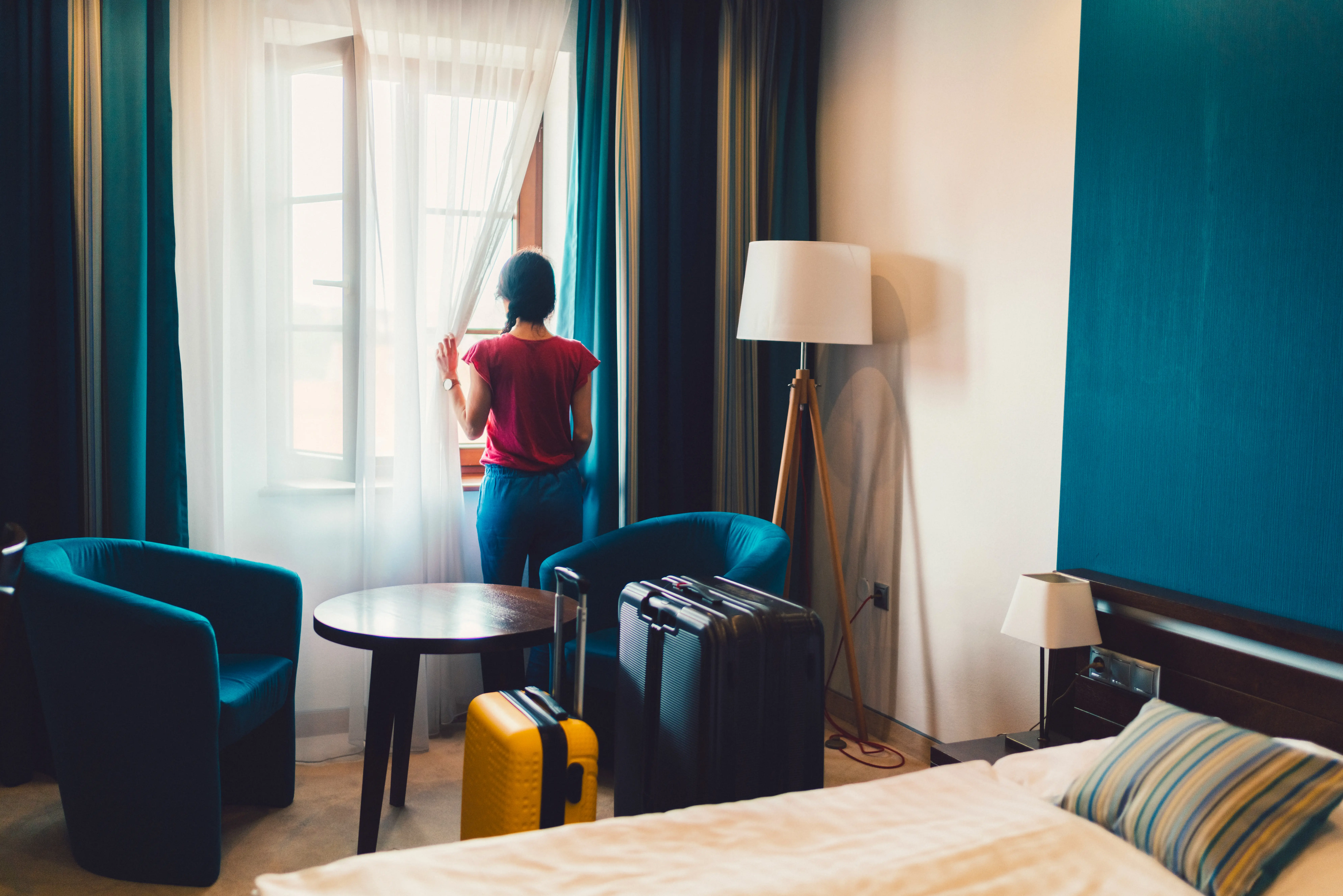 Young tourist woman just arriving in the hotel room and looking at nice view through the window