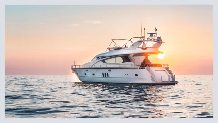 A yacht glides across the ocean as the sun sets behind it. 