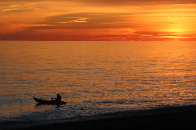 Image of a person kayaking at sunrise, silhouetted by the sunrise.
