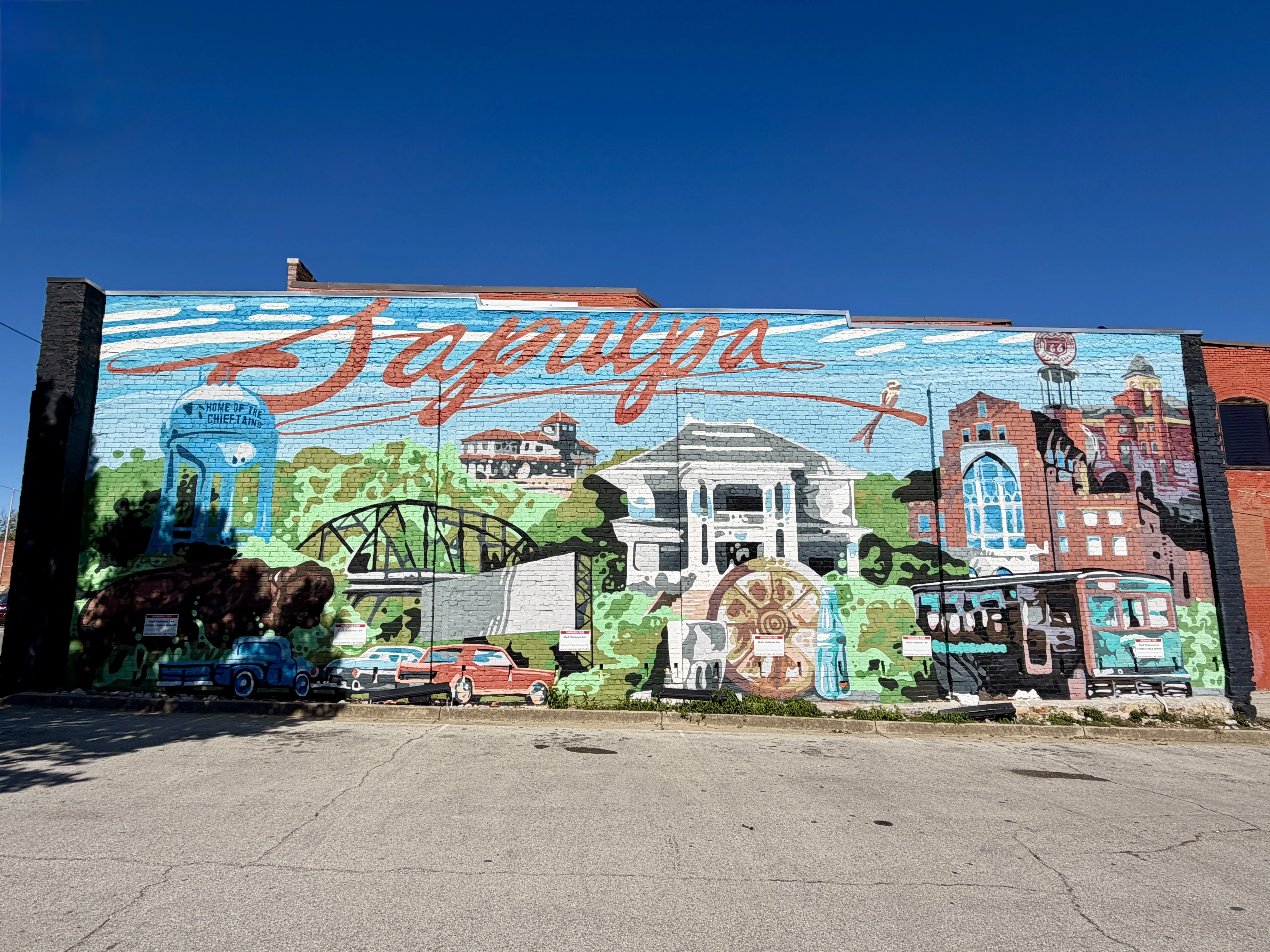 Mural painted on brick building representing Sapulpa with a trolley, water wheel, vintage cars, bridge and water tower