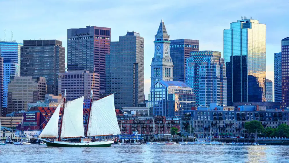 A sailboat in the Boston Harbor with a view of Downtown Boston skyline in the background.