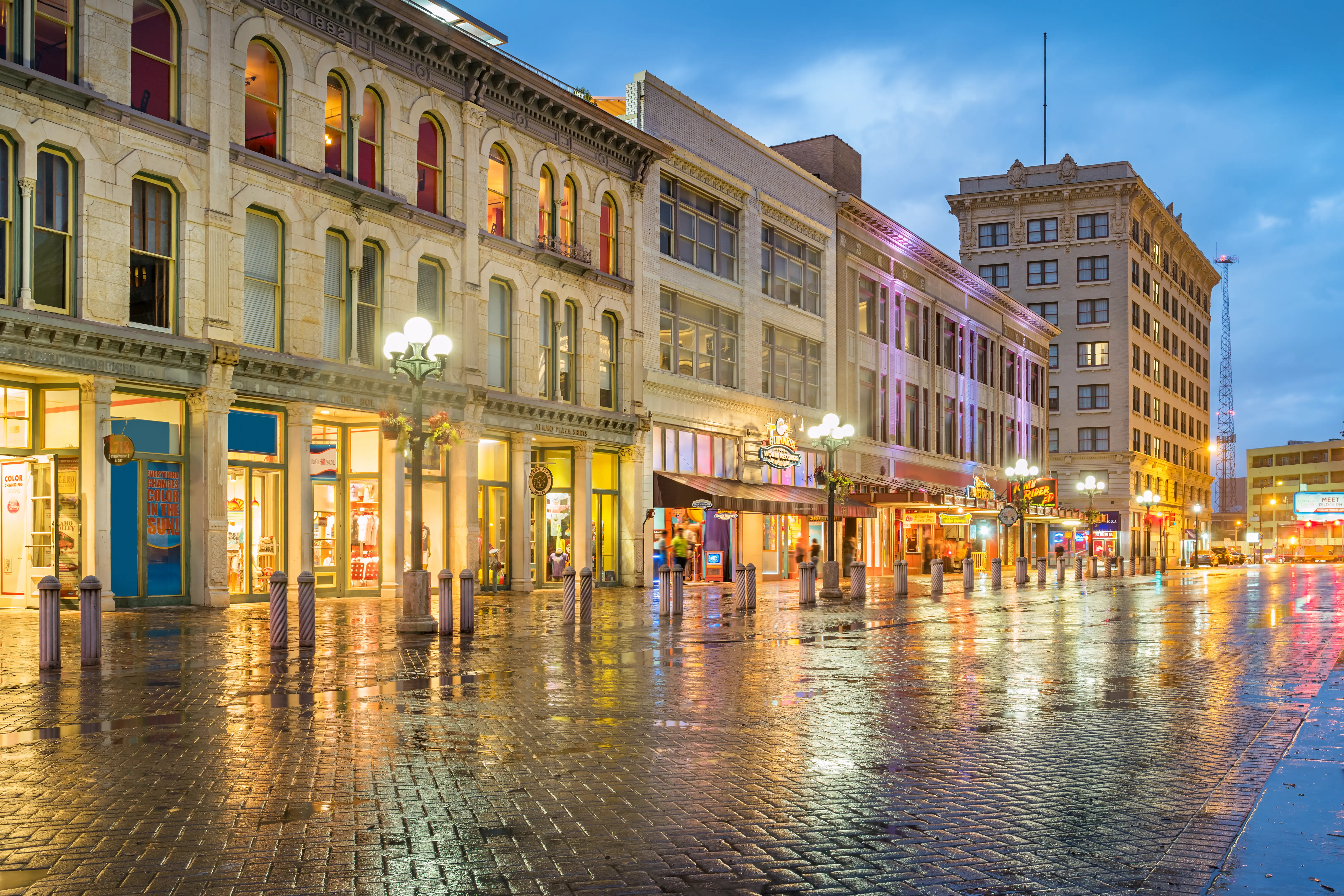 Stock photograph of colorful businesses in Alamo Plaza shopping district in downtown San Antonio Texas at twilight blue hour.