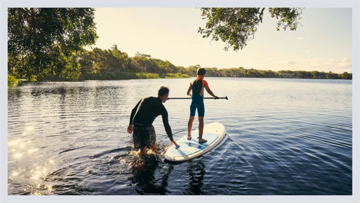 A young boy and his dad are shown paddleboarding on a clear lake. 