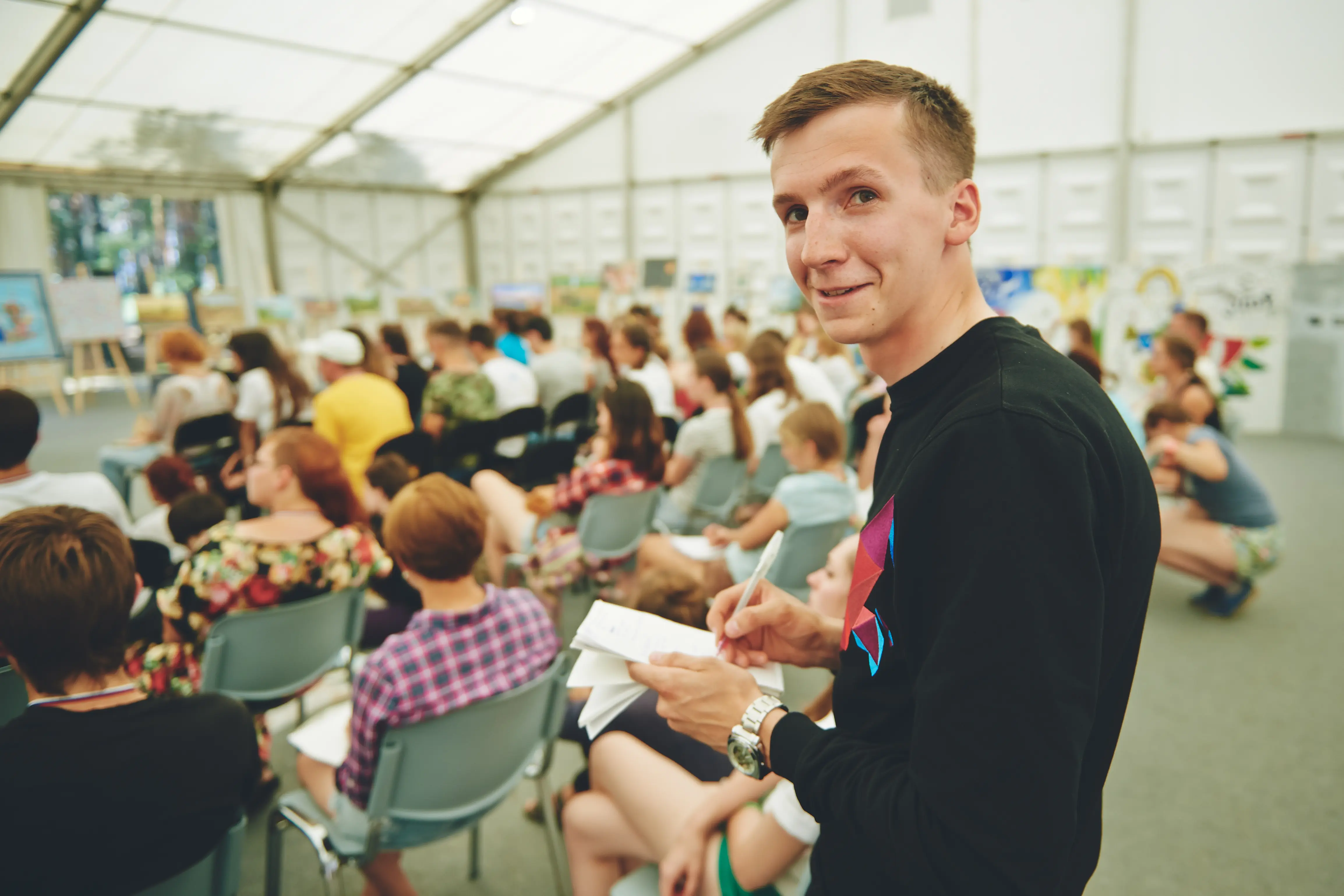 Image of a man at a public event taking notes on a notepad.