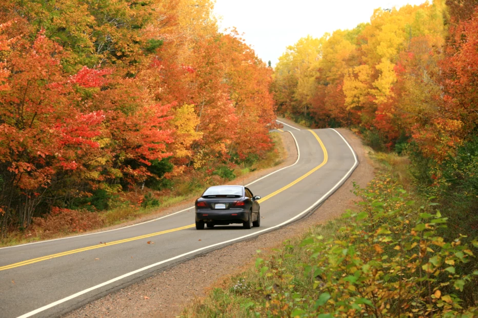 Car traveling on a two-lane road surrounded by colorful fall leaves.